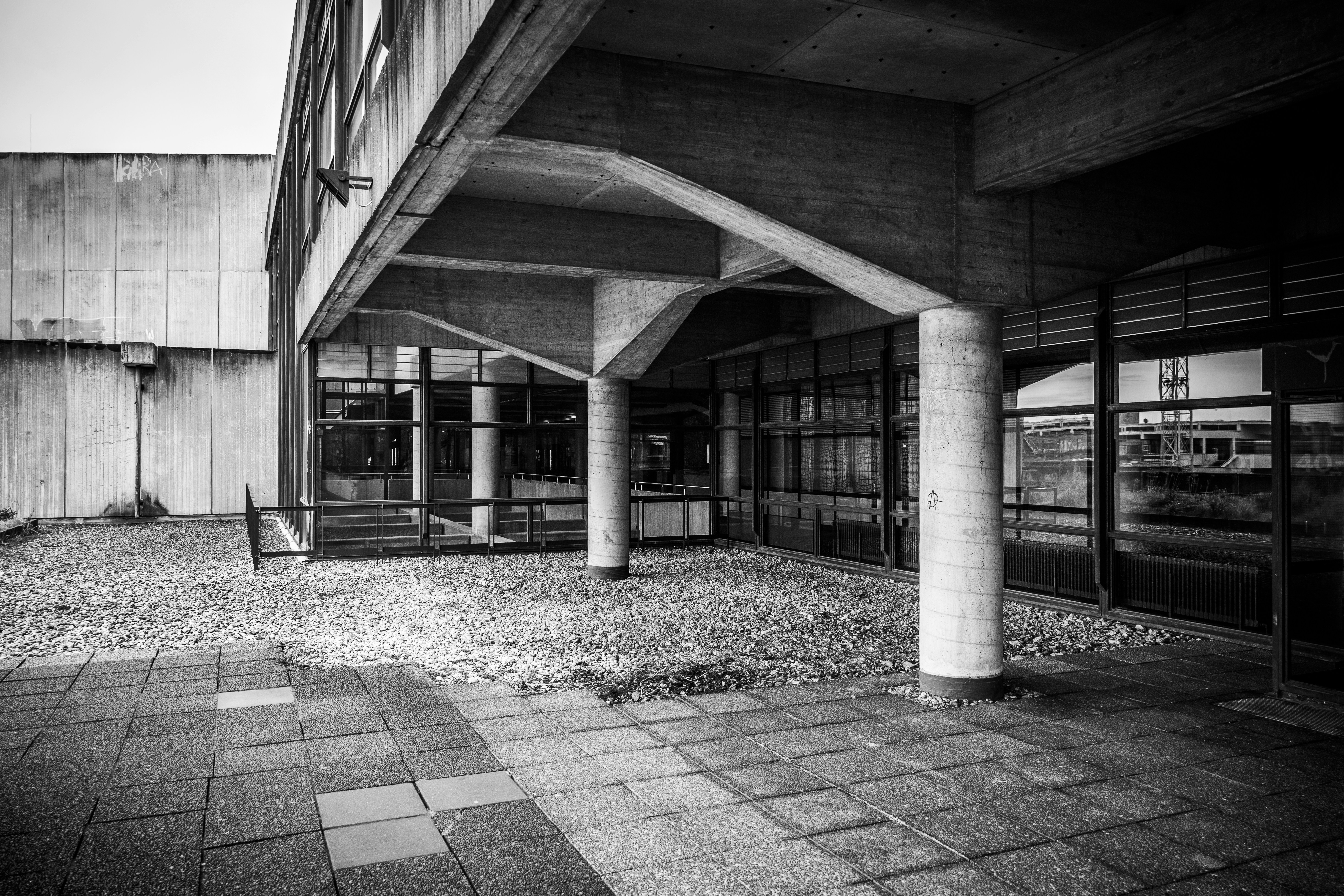 Concrete building entrance with large windows and gravel courtyard