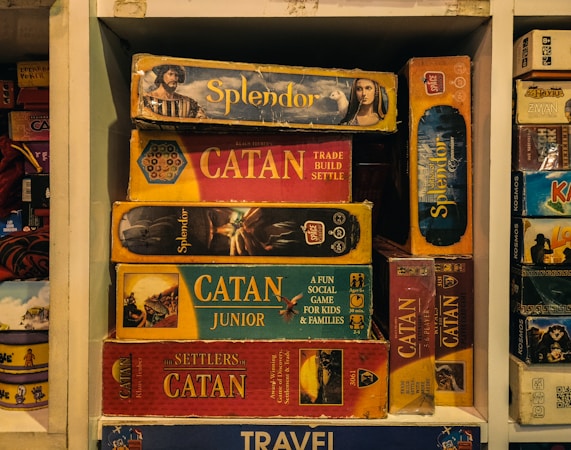 Stack of board games including Catan on a shelf