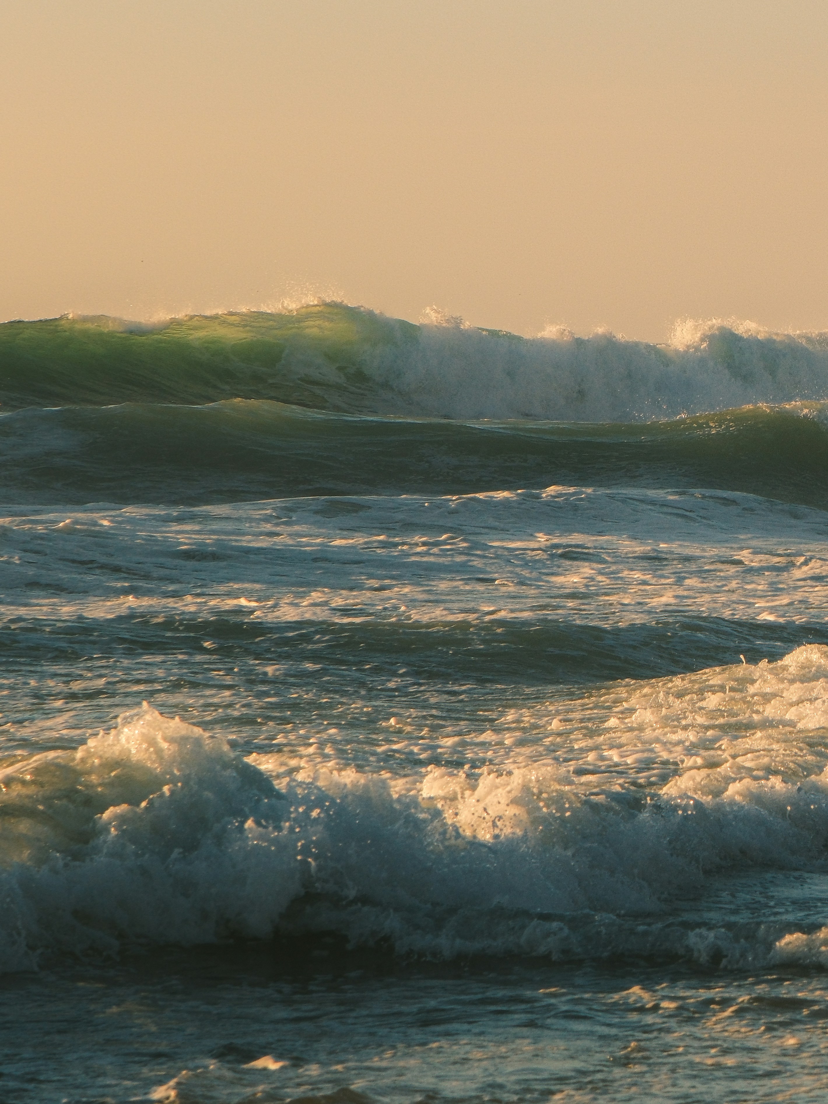 Photo of Ocean waves crashing under a warm sky by Kellen Riggin
