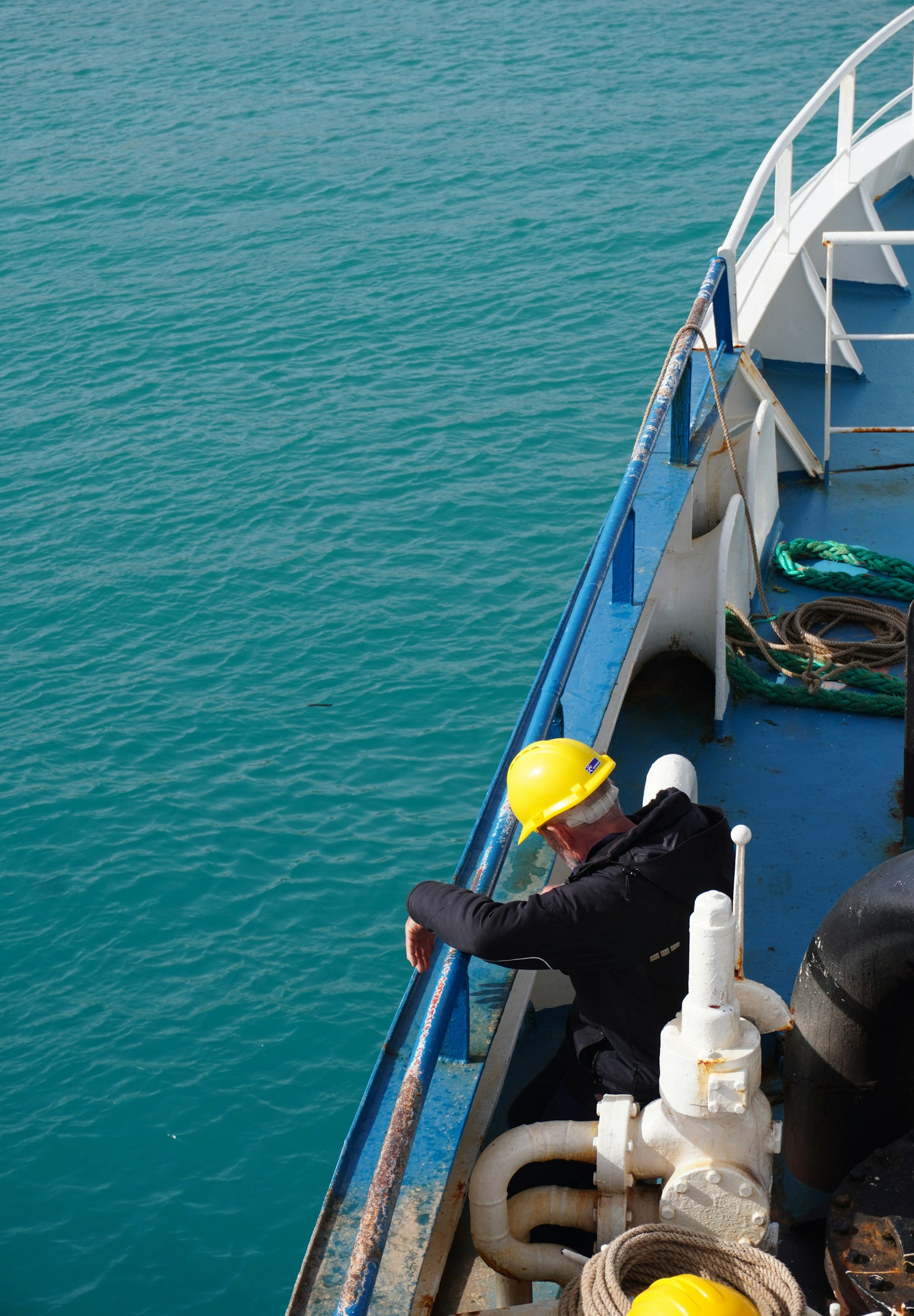 Man in hard hat on a ship deck overlooking ocean.