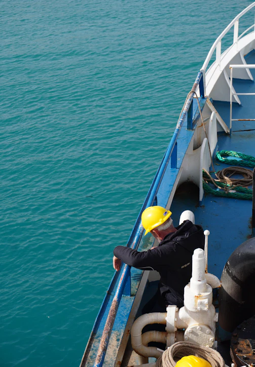 Man in hard hat on a ship deck overlooking ocean.