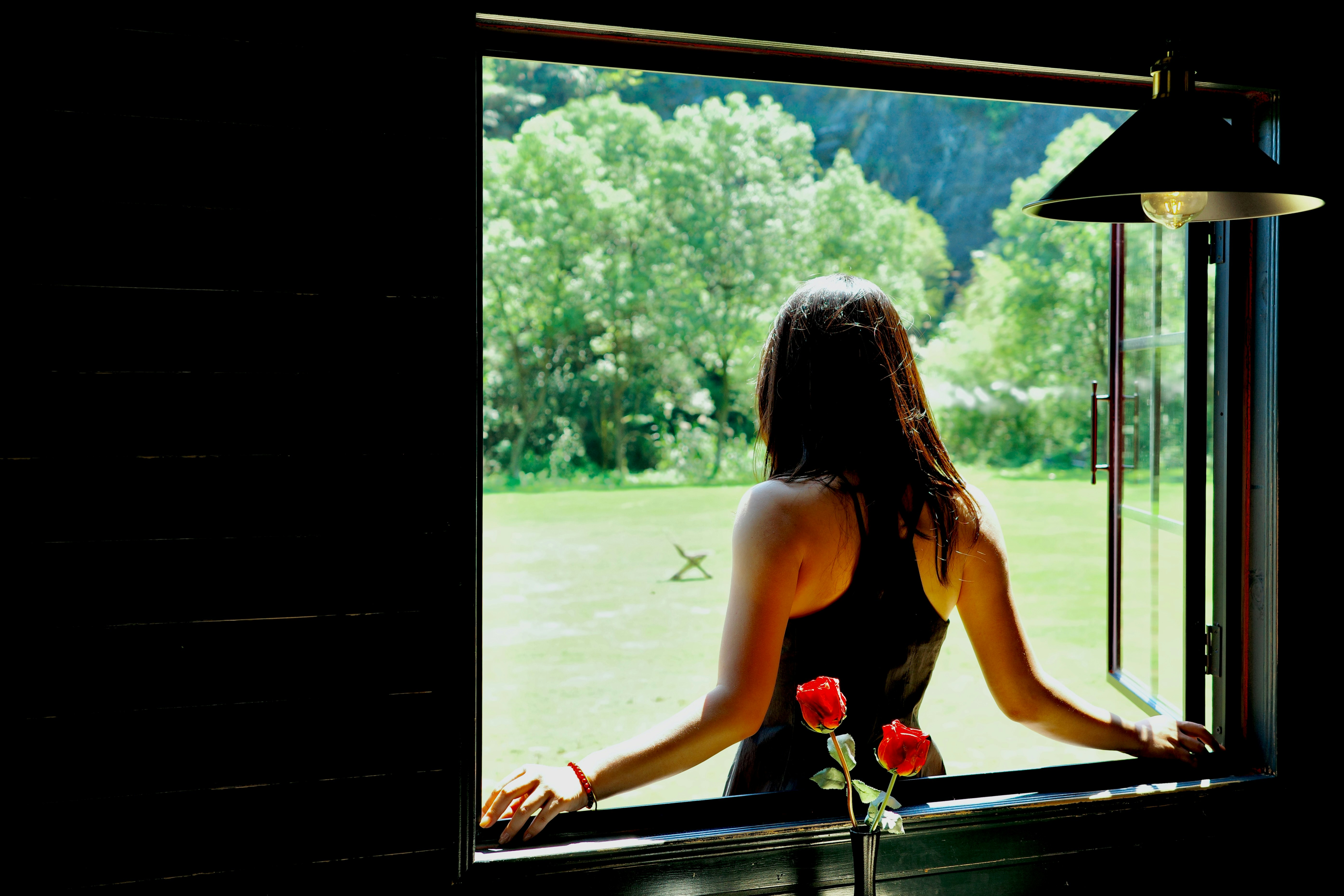 A woman looking out an open window at greenery, reflecting quietly during a lower-capacity phase of her cycle.