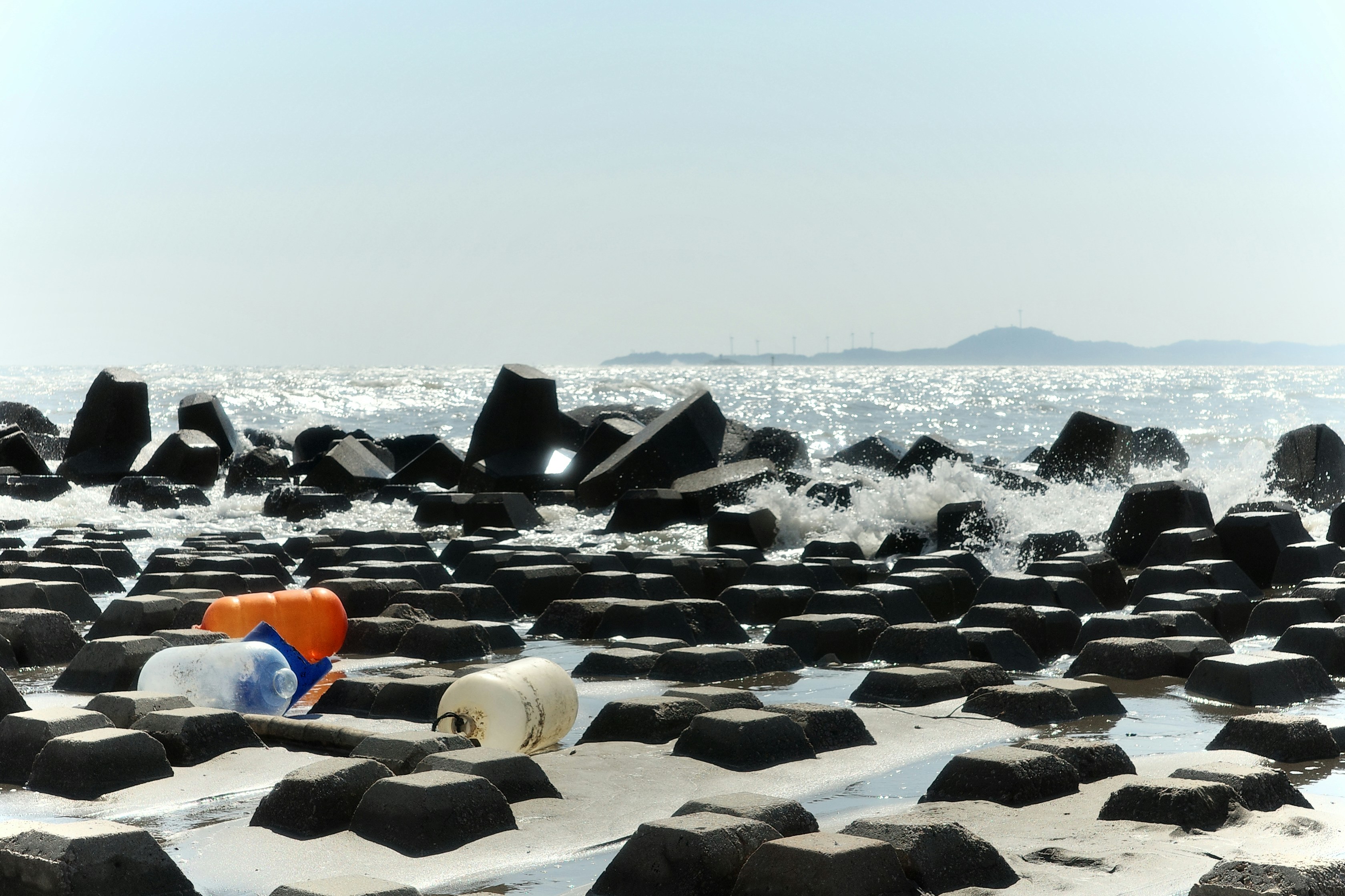 Plastic bottles litter a rocky shoreline with ocean waves.