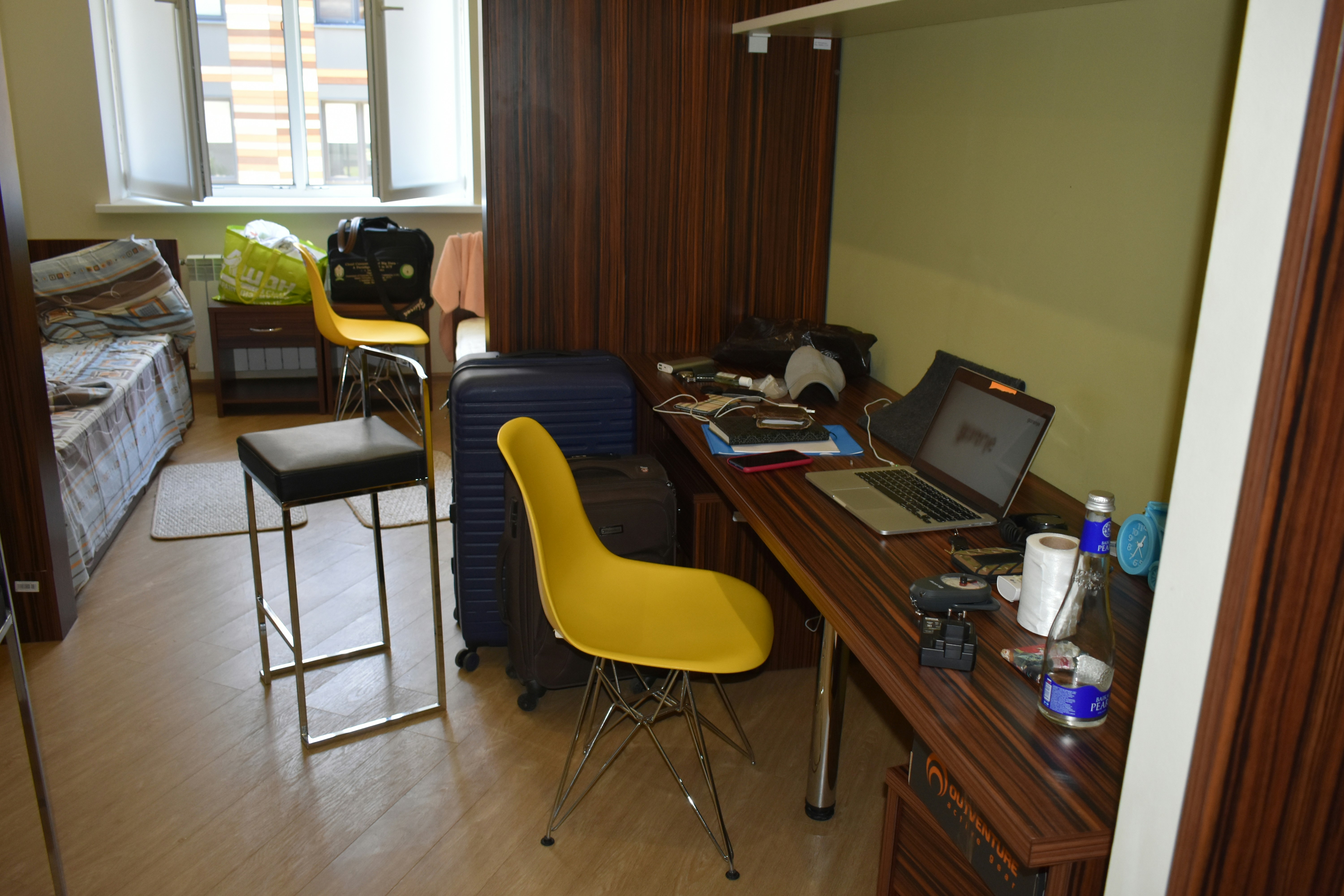 A cluttered room with a desk, chairs, and luggage.