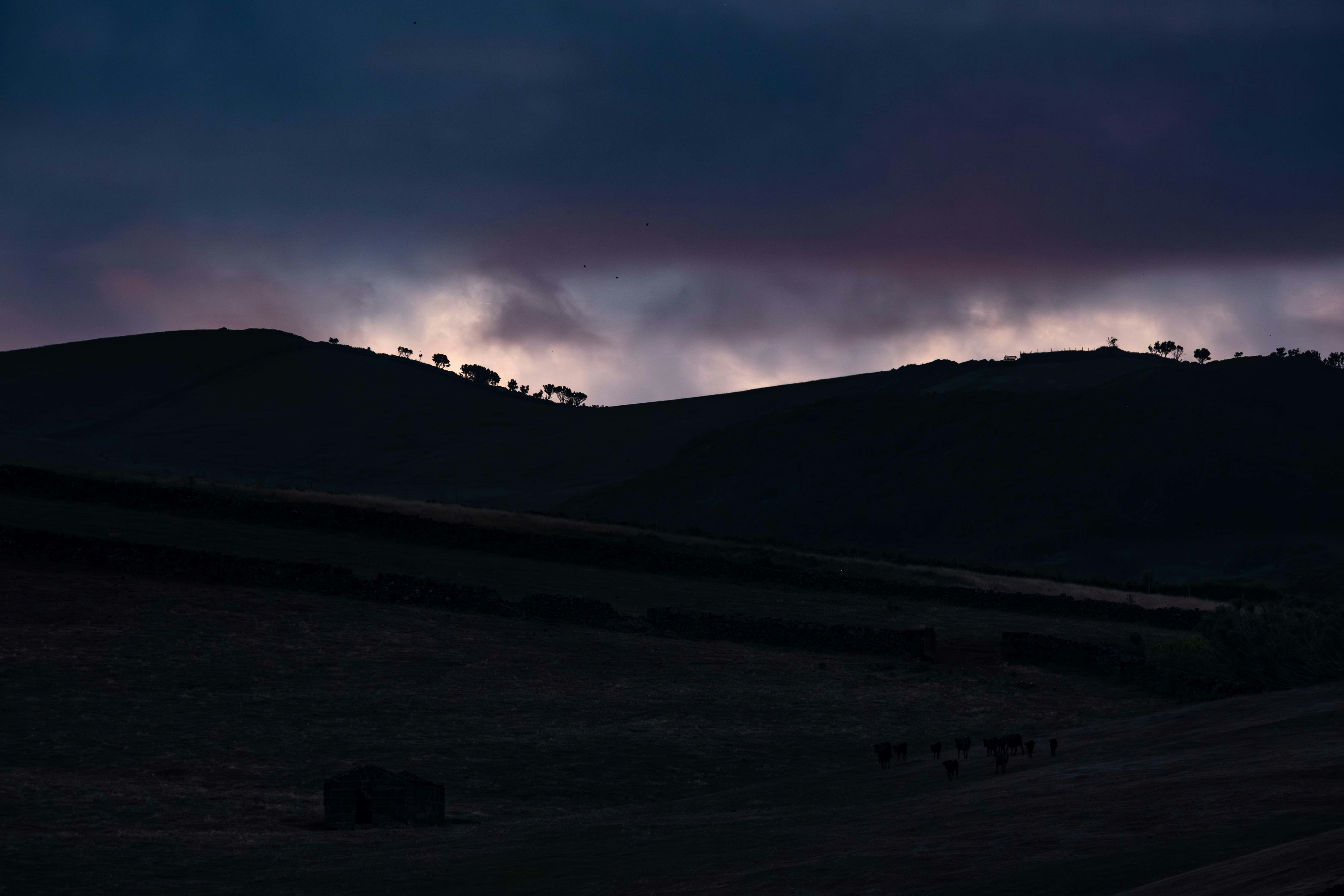 Dark rolling hills at dusk with colorful clouds