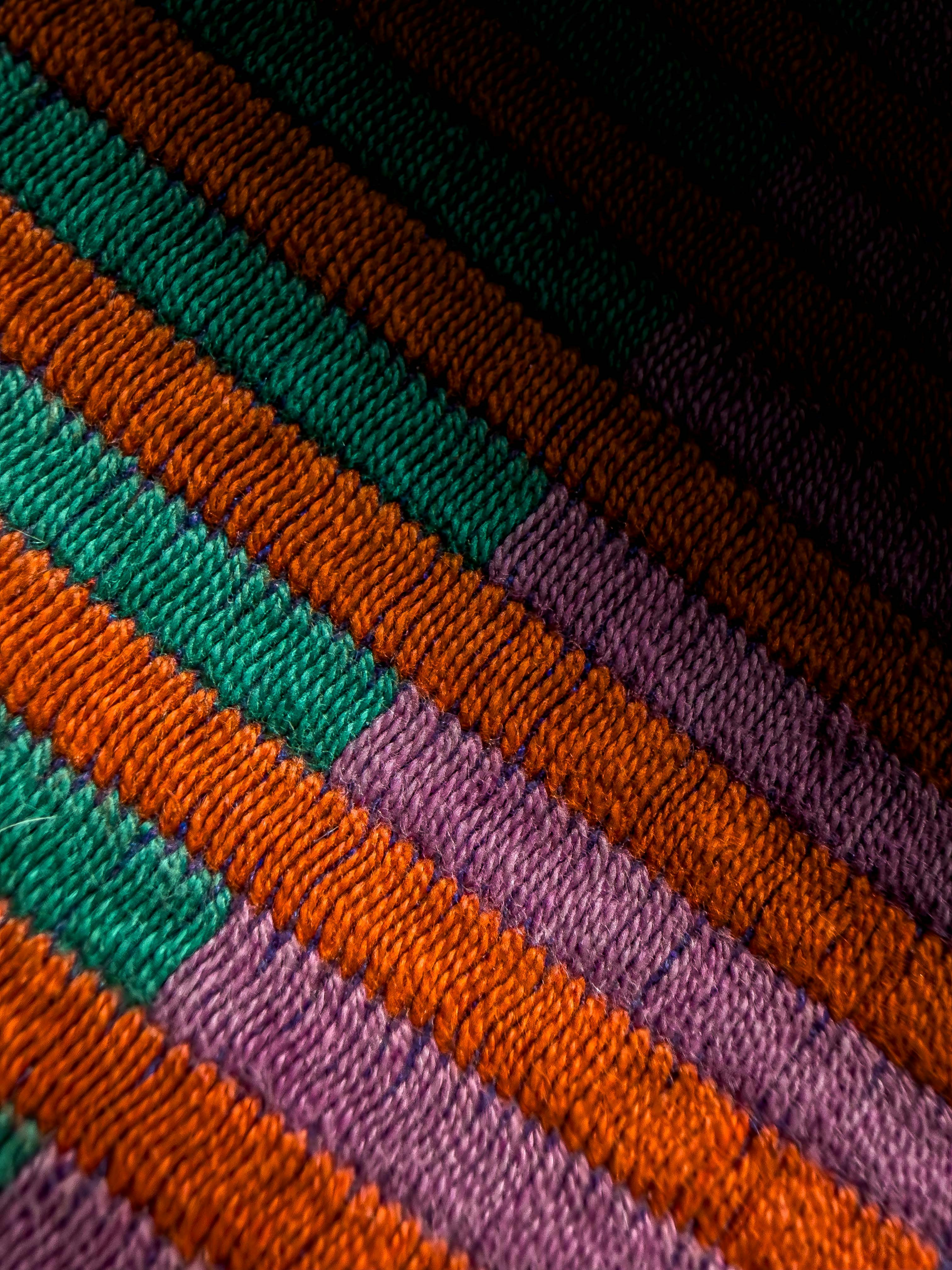 Diagonal stripes of purple, orange, green, and brown yarn.
