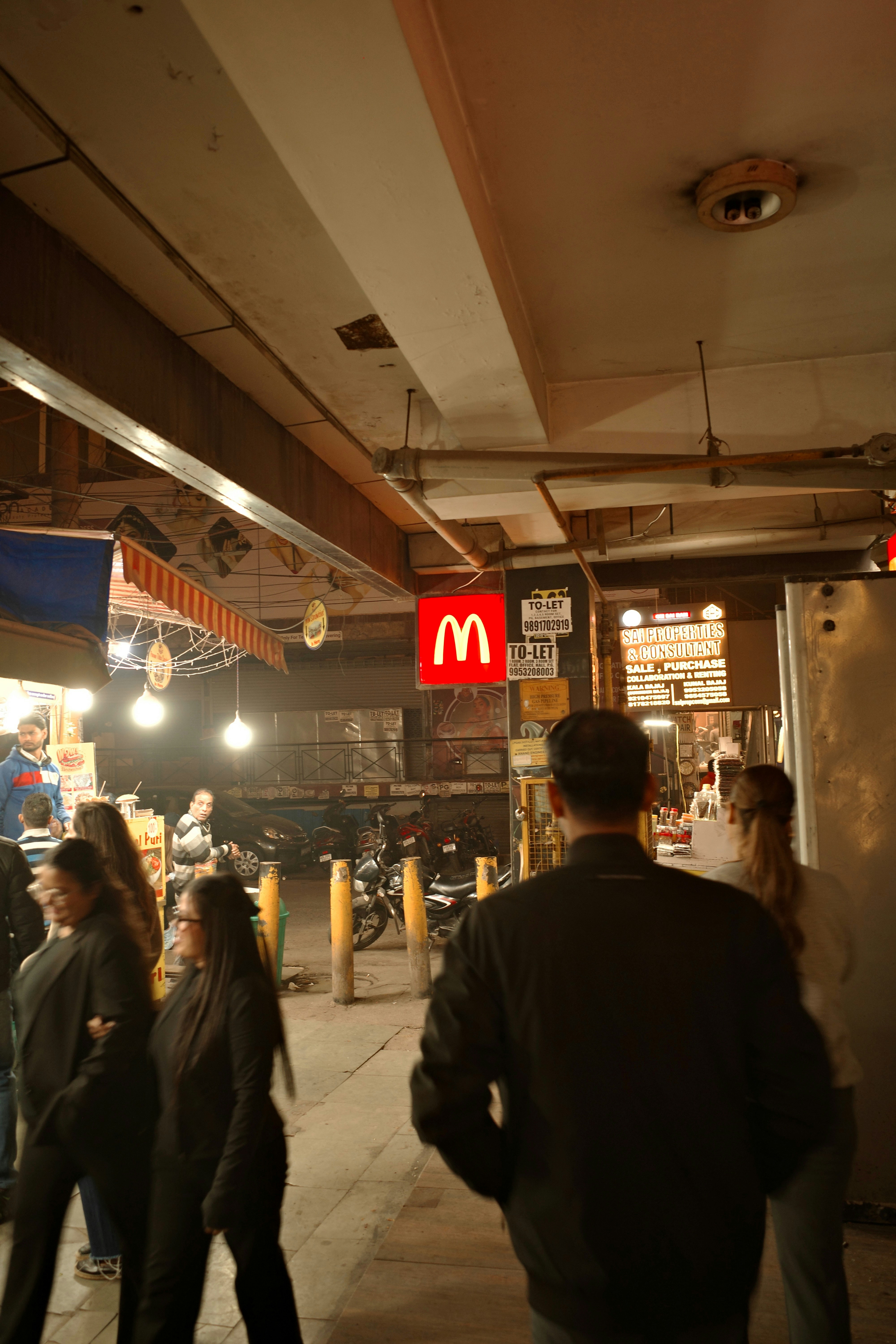 People walking past a mcdonald's sign at night.