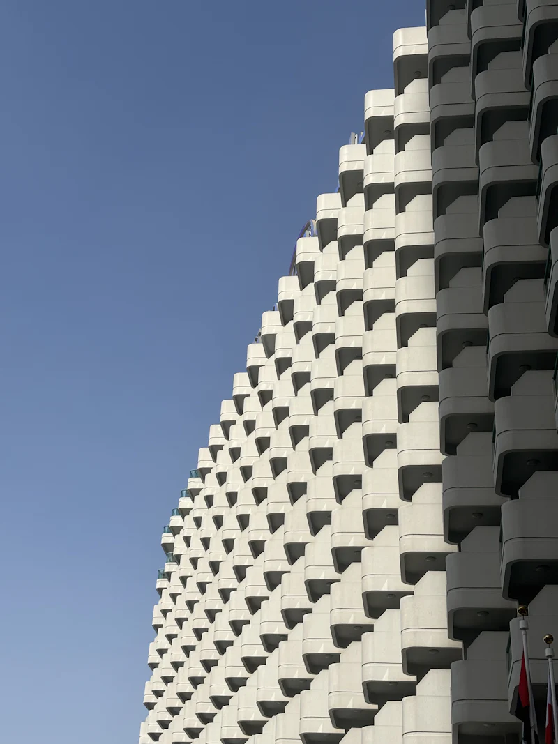 white building facade of stacked balconies against a clear blue sky