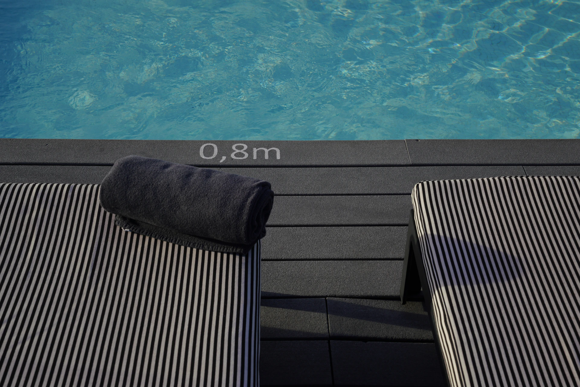 Two lounge chairs by a swimming pool with a towel.