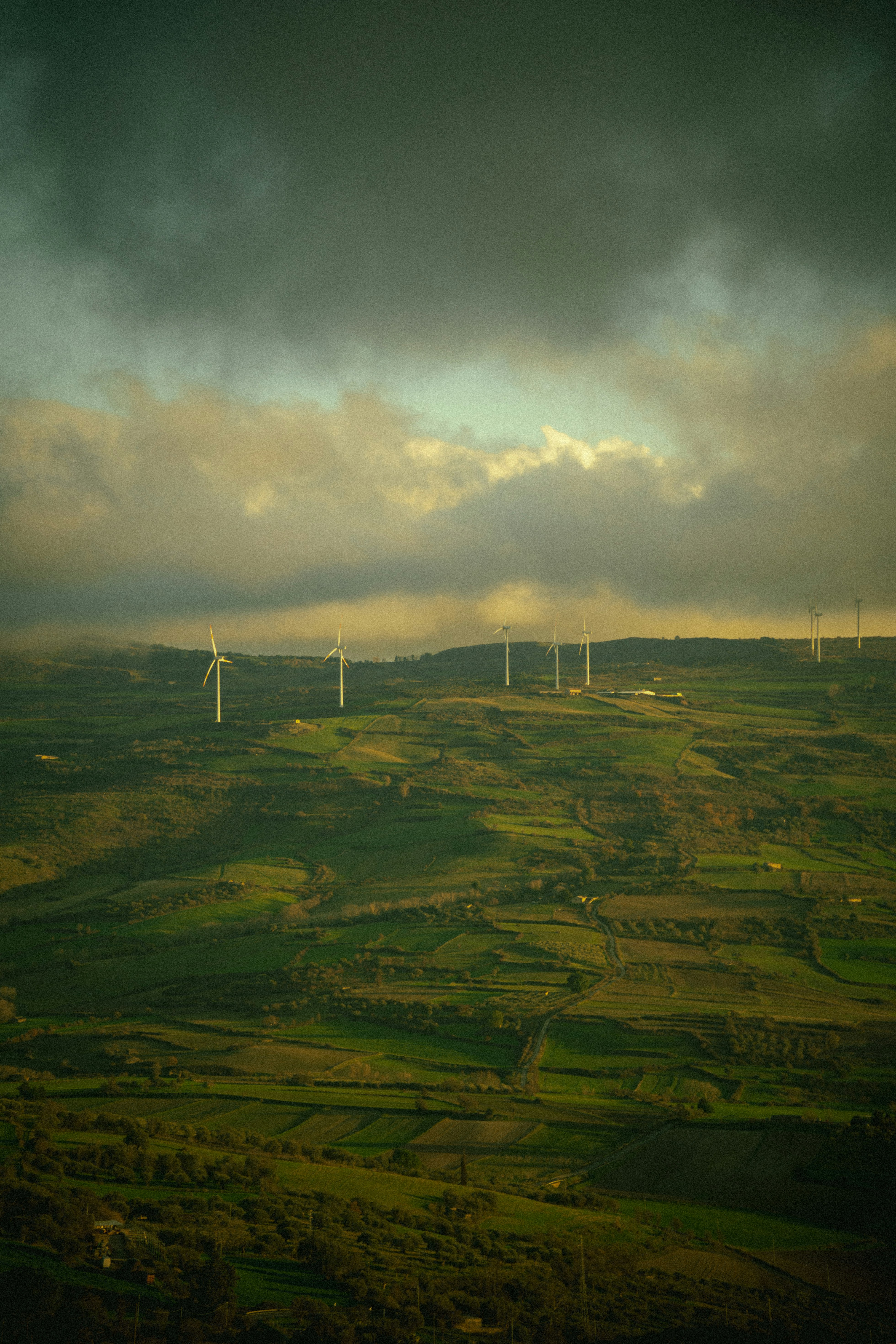 Aerogeneradores salpicando un paisaje verde y montañoso bajo un cielo nublado