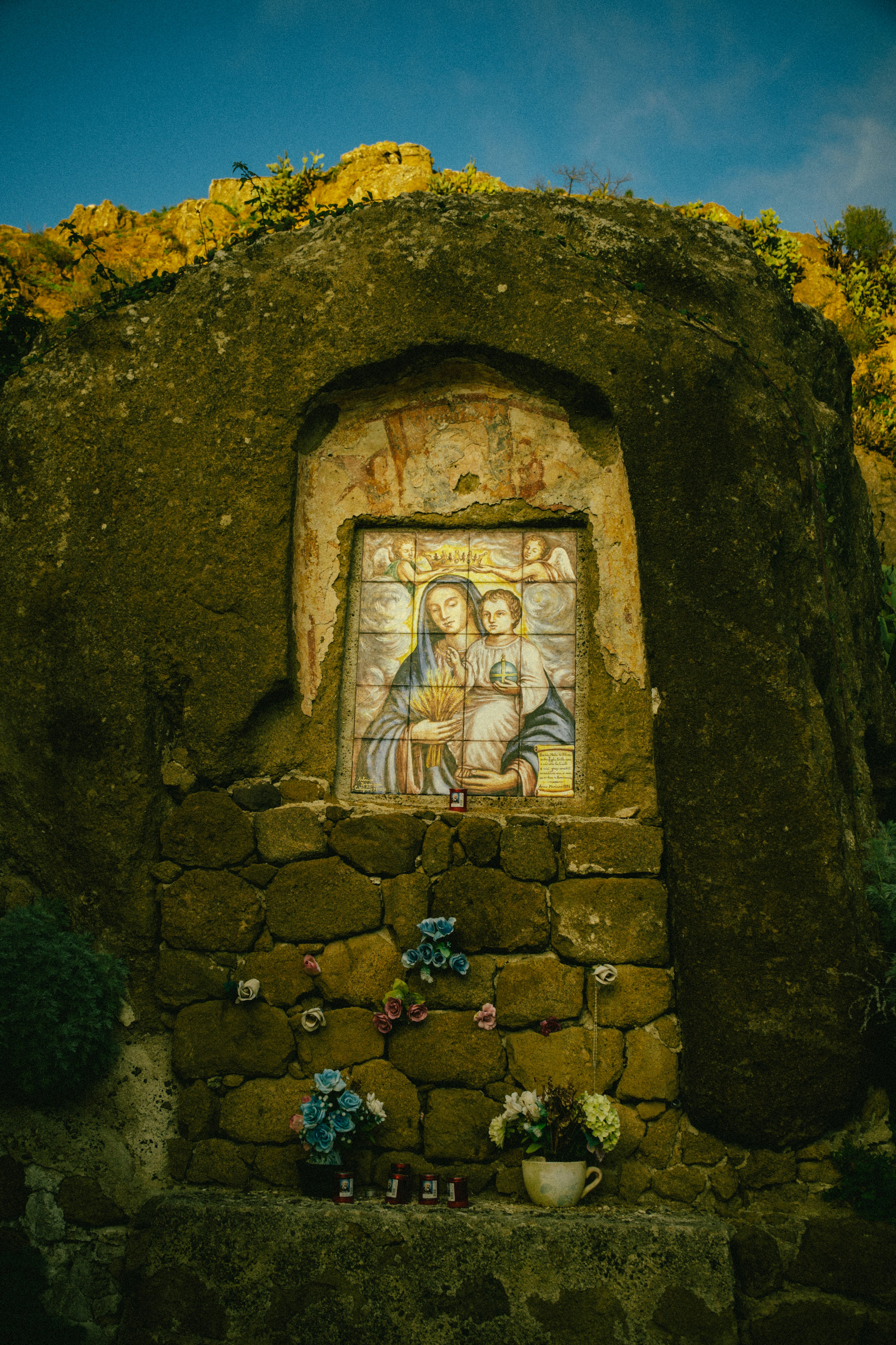 Mosaico religioso de la Madonna con el Niño en nicho de roca.