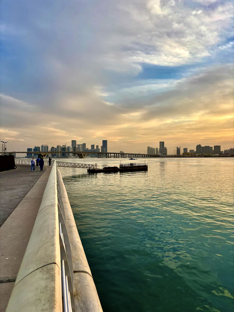 waterfront promenade railing at sunset with a skyline across the water