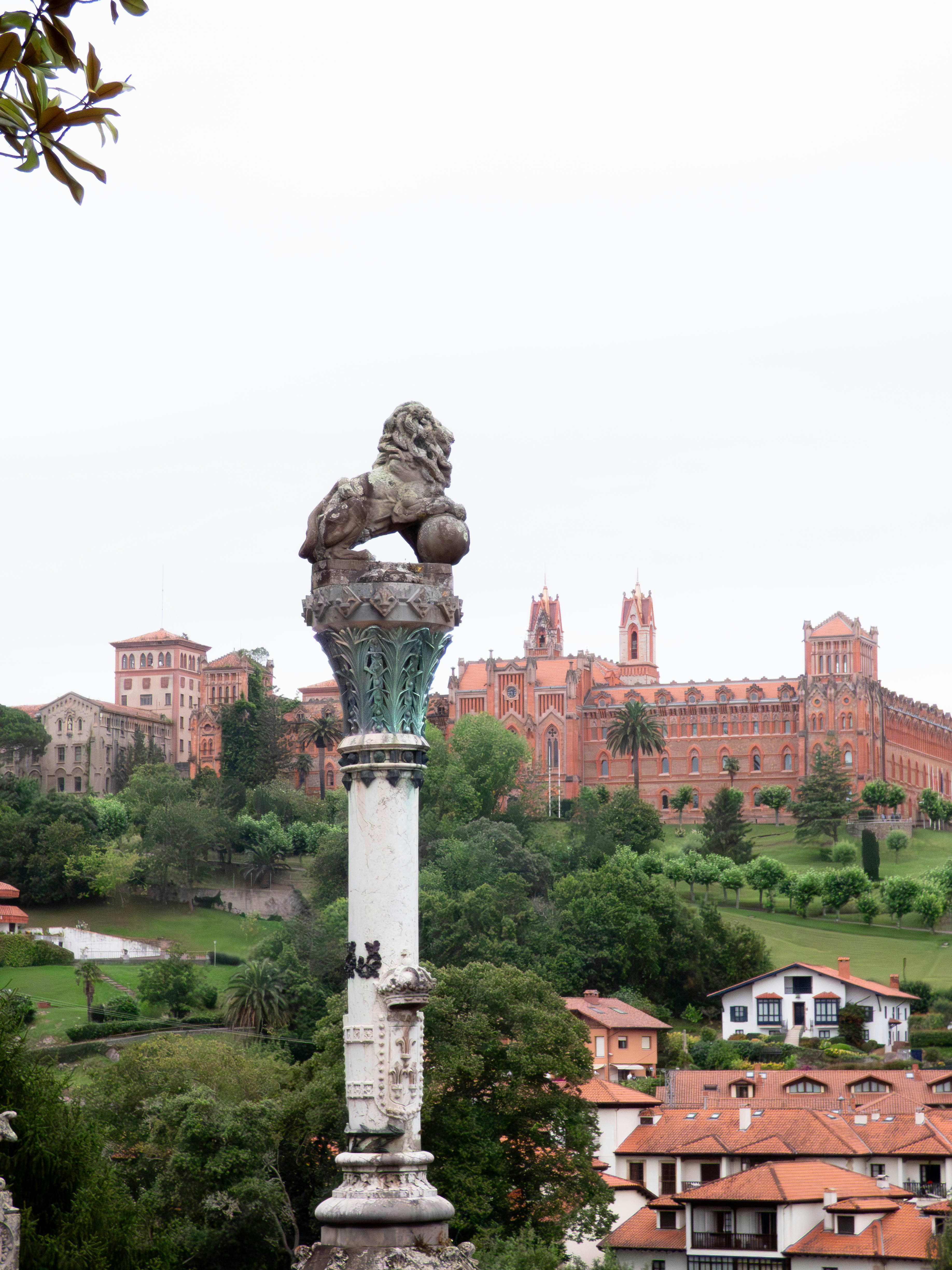 Stone lion sculpture with buildings on a hill.