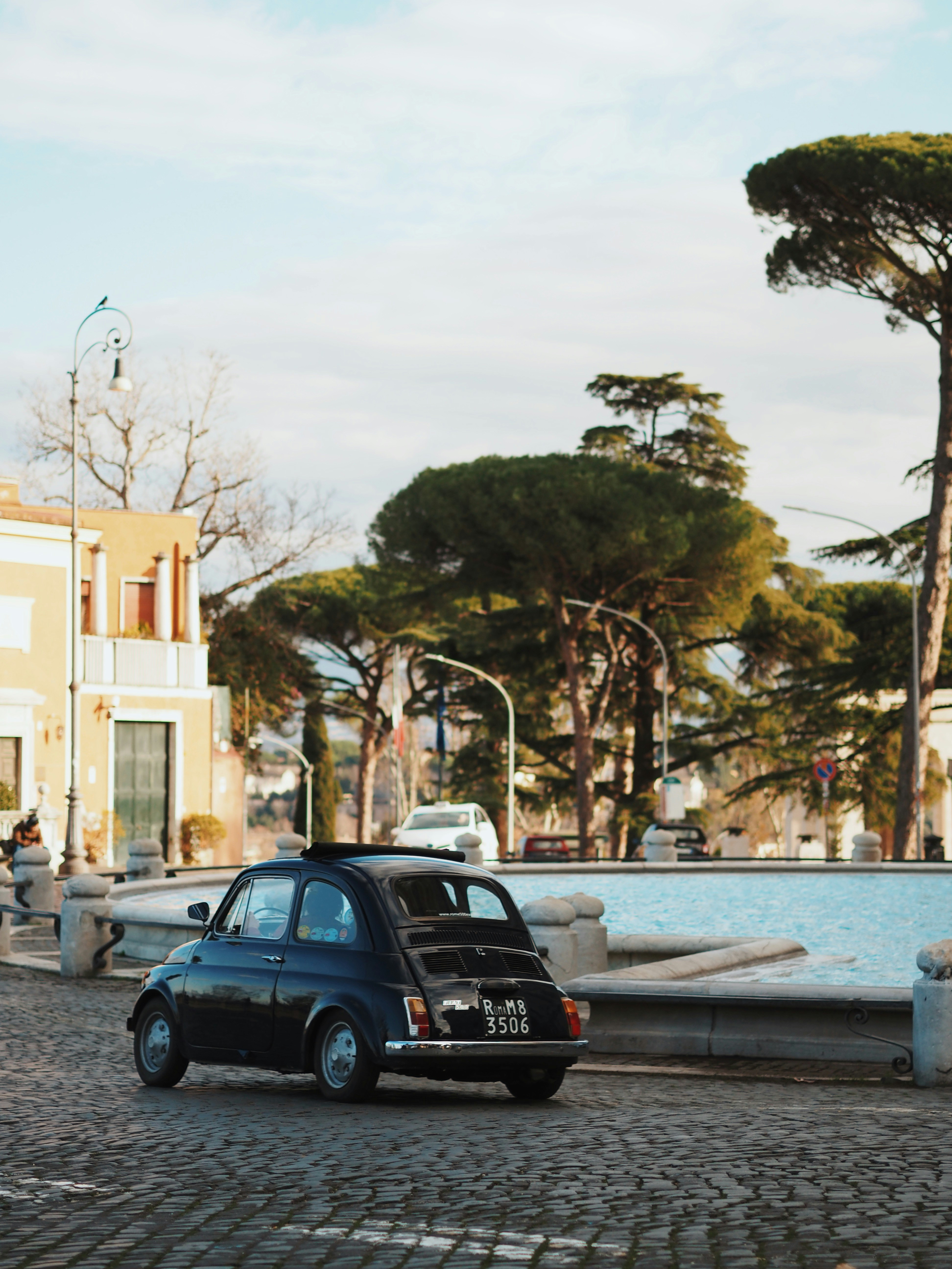 A vintage black fiat 500 car on cobblestone street.