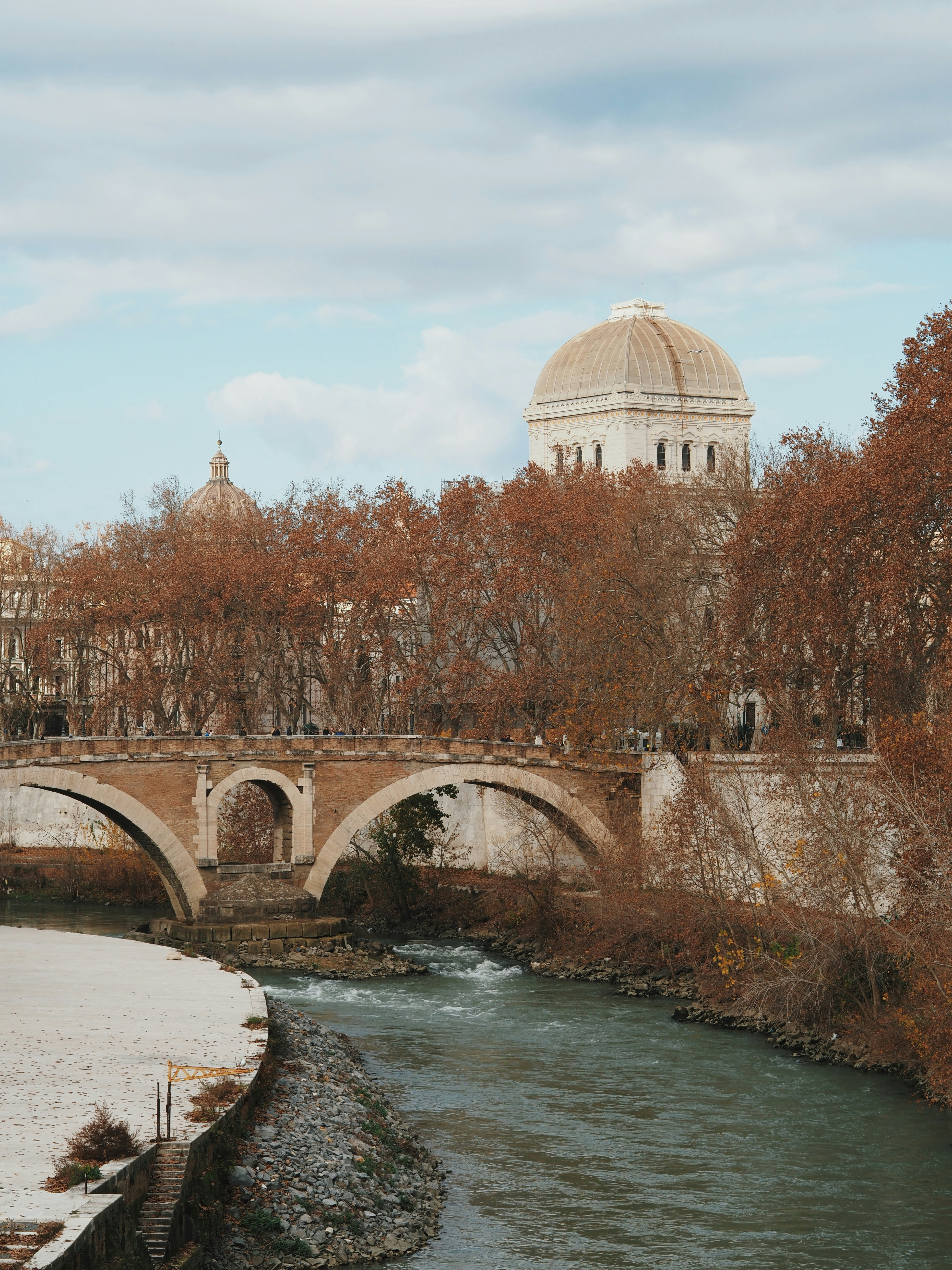 Stone bridge over a river with autumn trees and buildings.