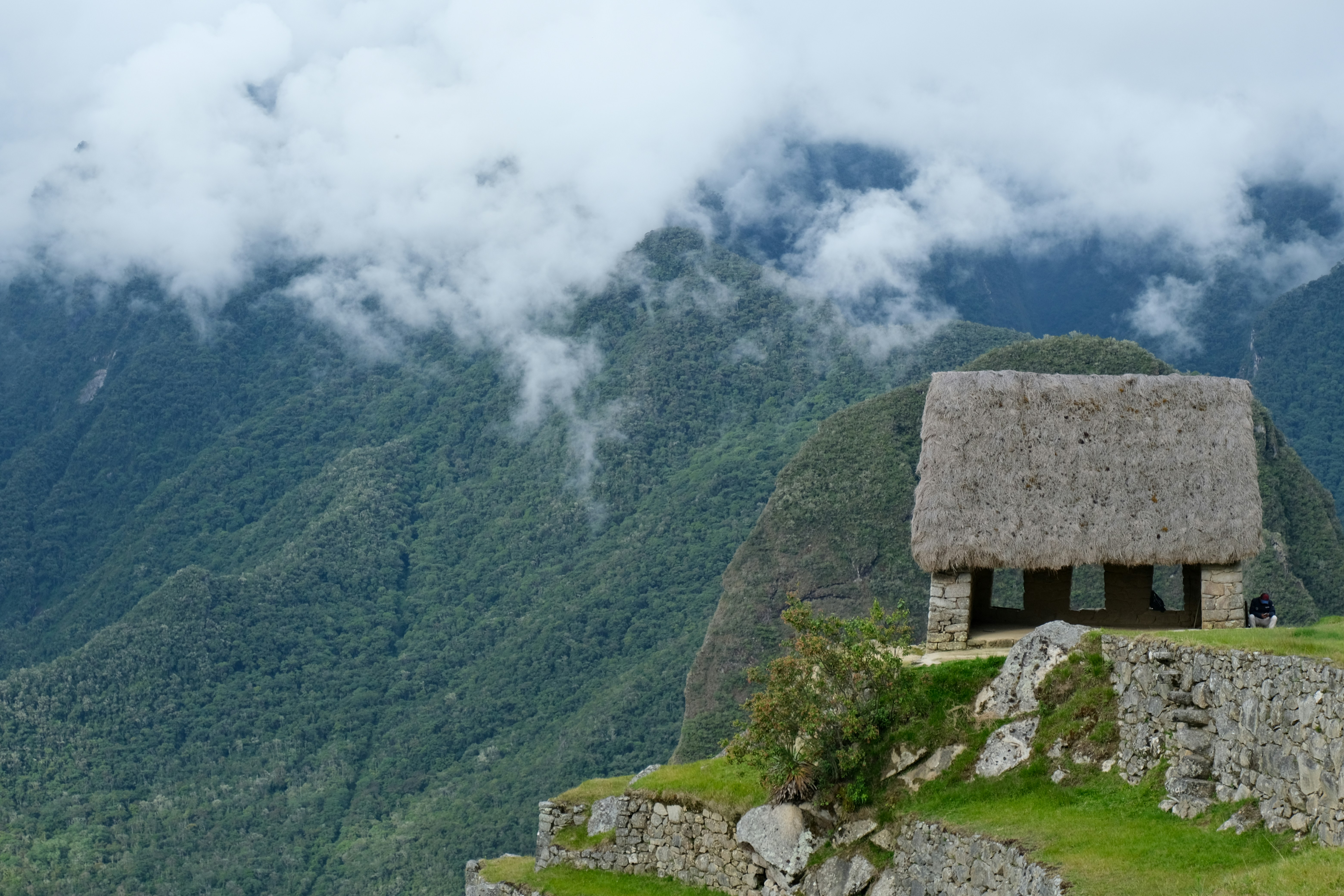 Thatched roof building on a mountainside with clouds.