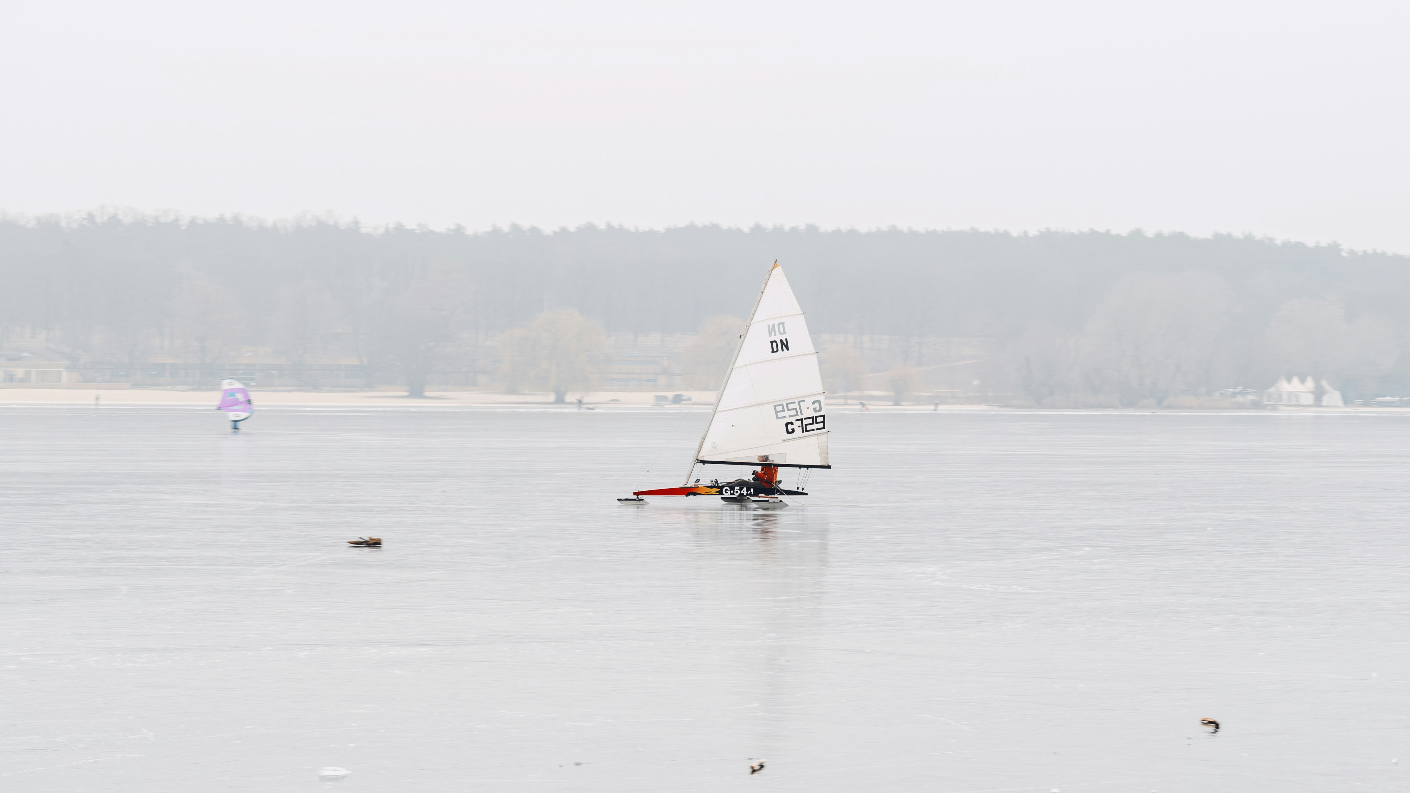A small sailboat navigates a calm, overcast lake.