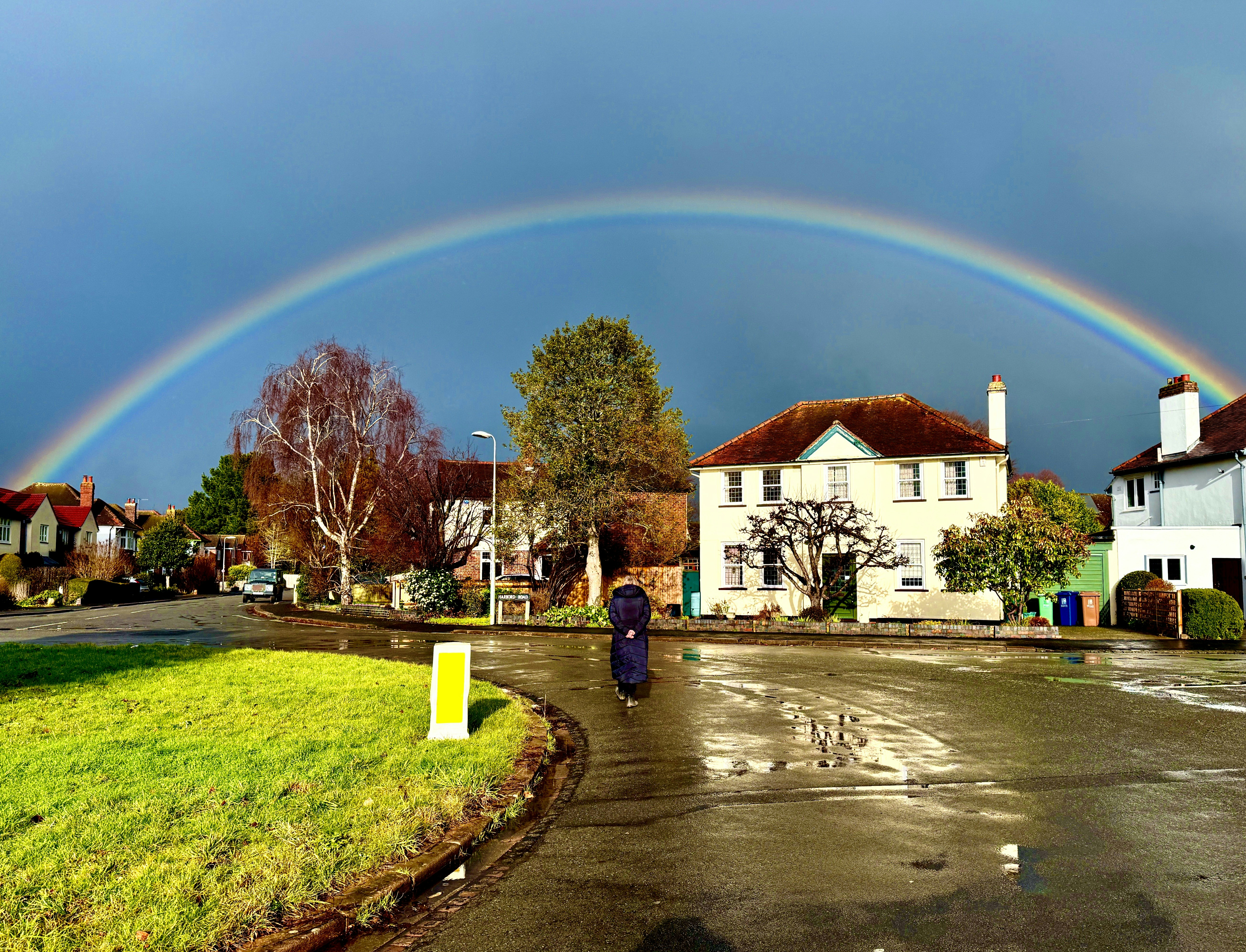 A vibrant rainbow arches over a suburban street after rain.