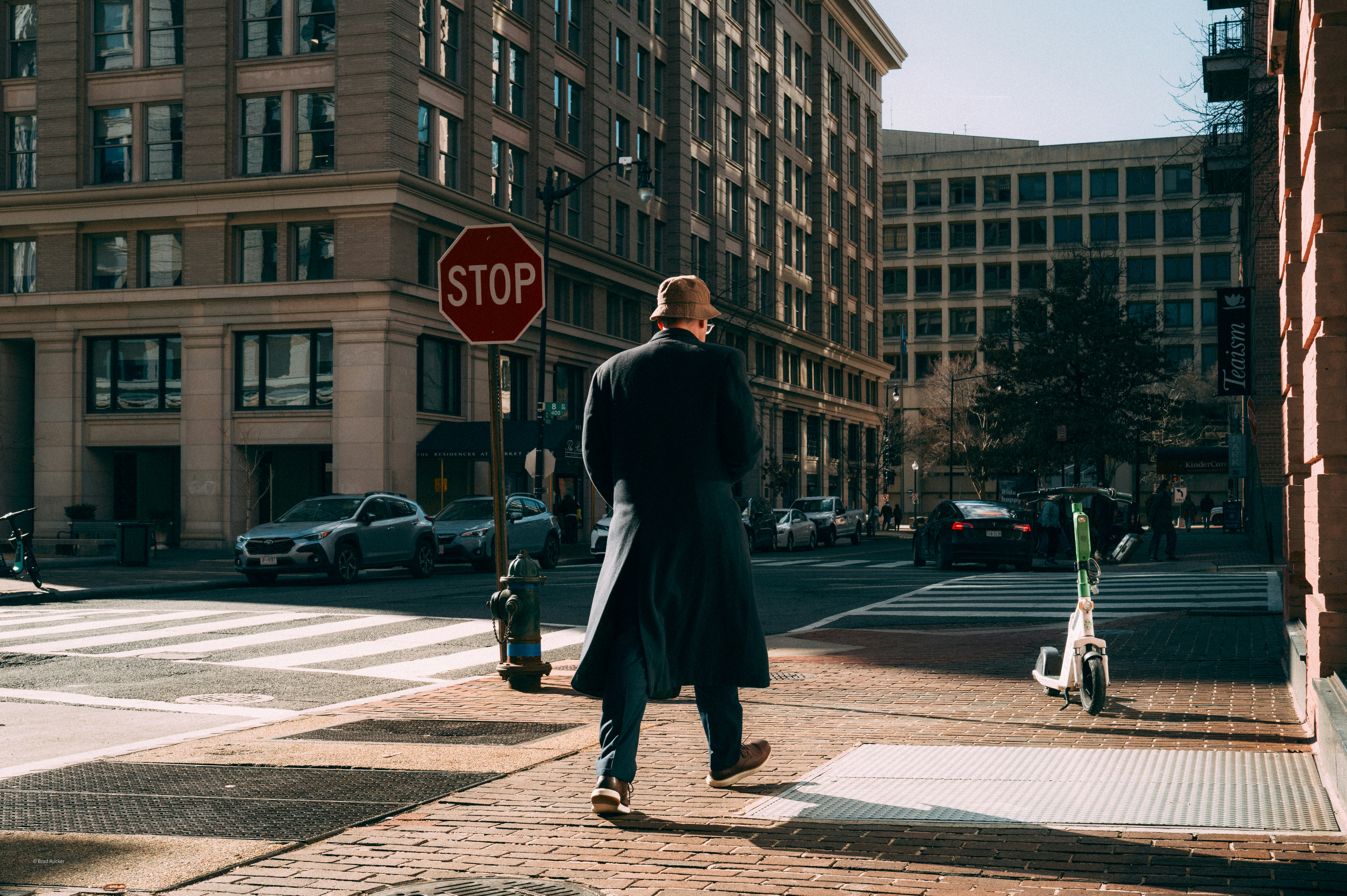 Man in trench coat walks past stop sign.