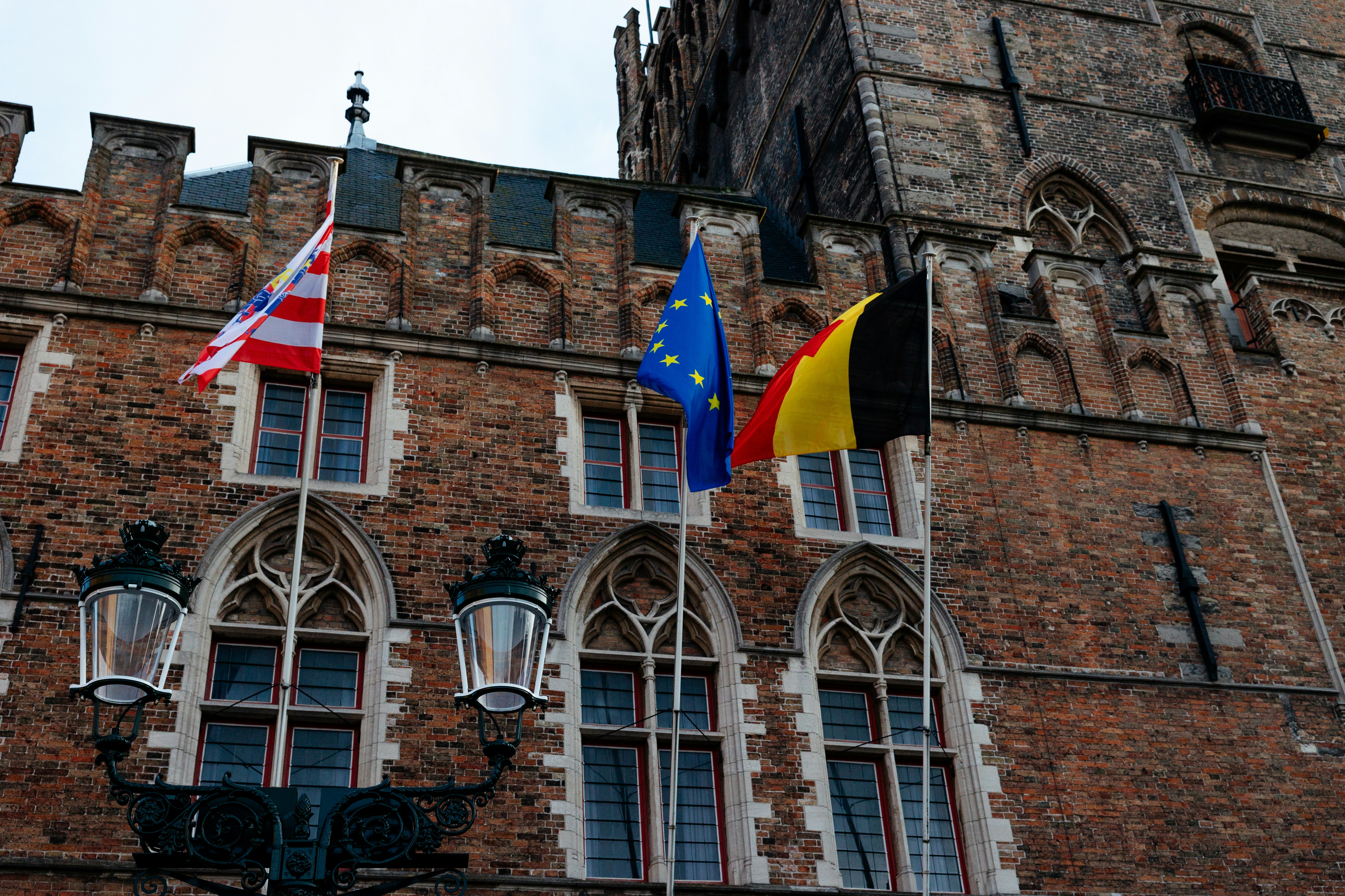 Three flags fly in front of a brick building.