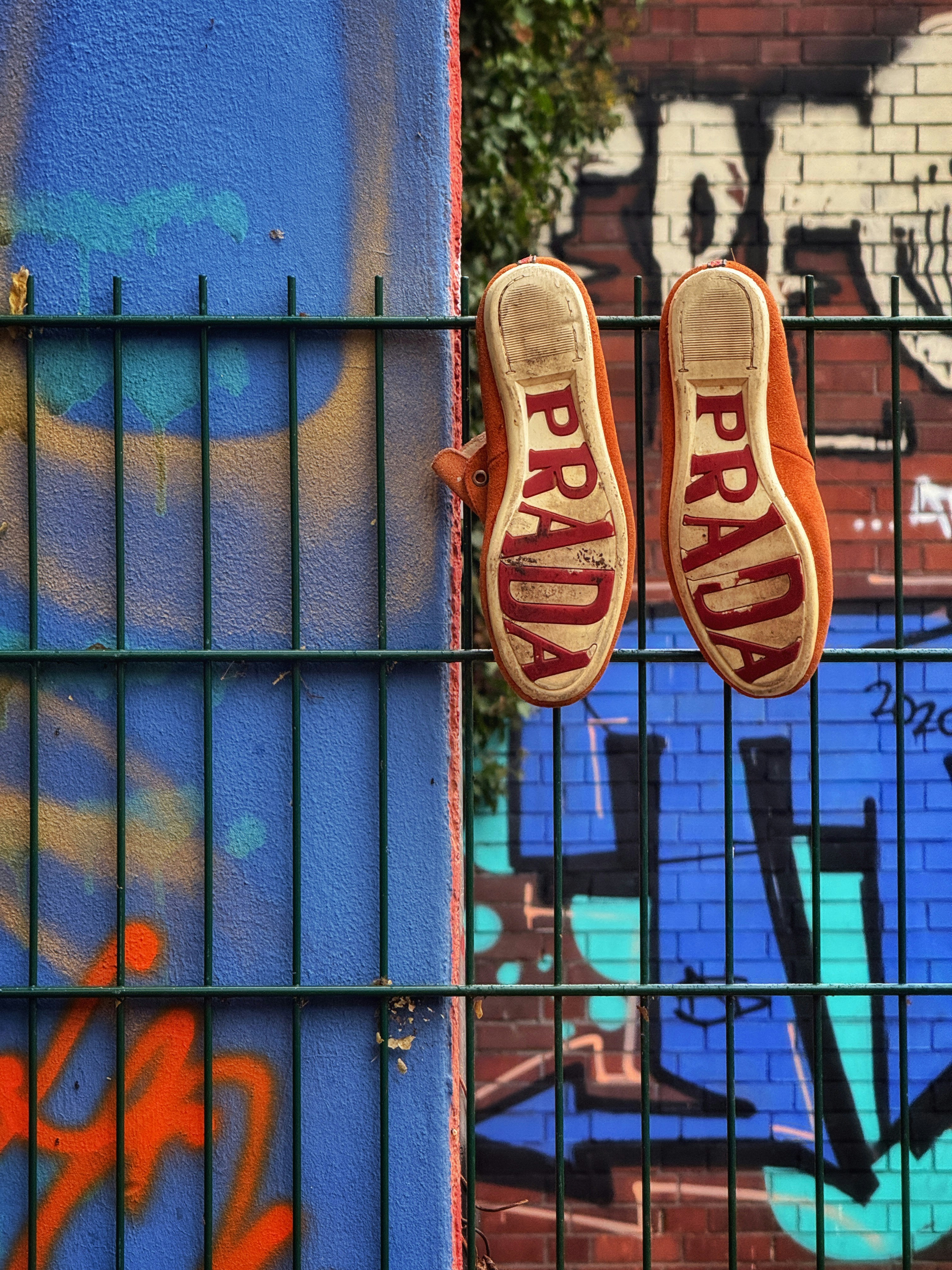 Orange shoes with prada logo hanging on fence