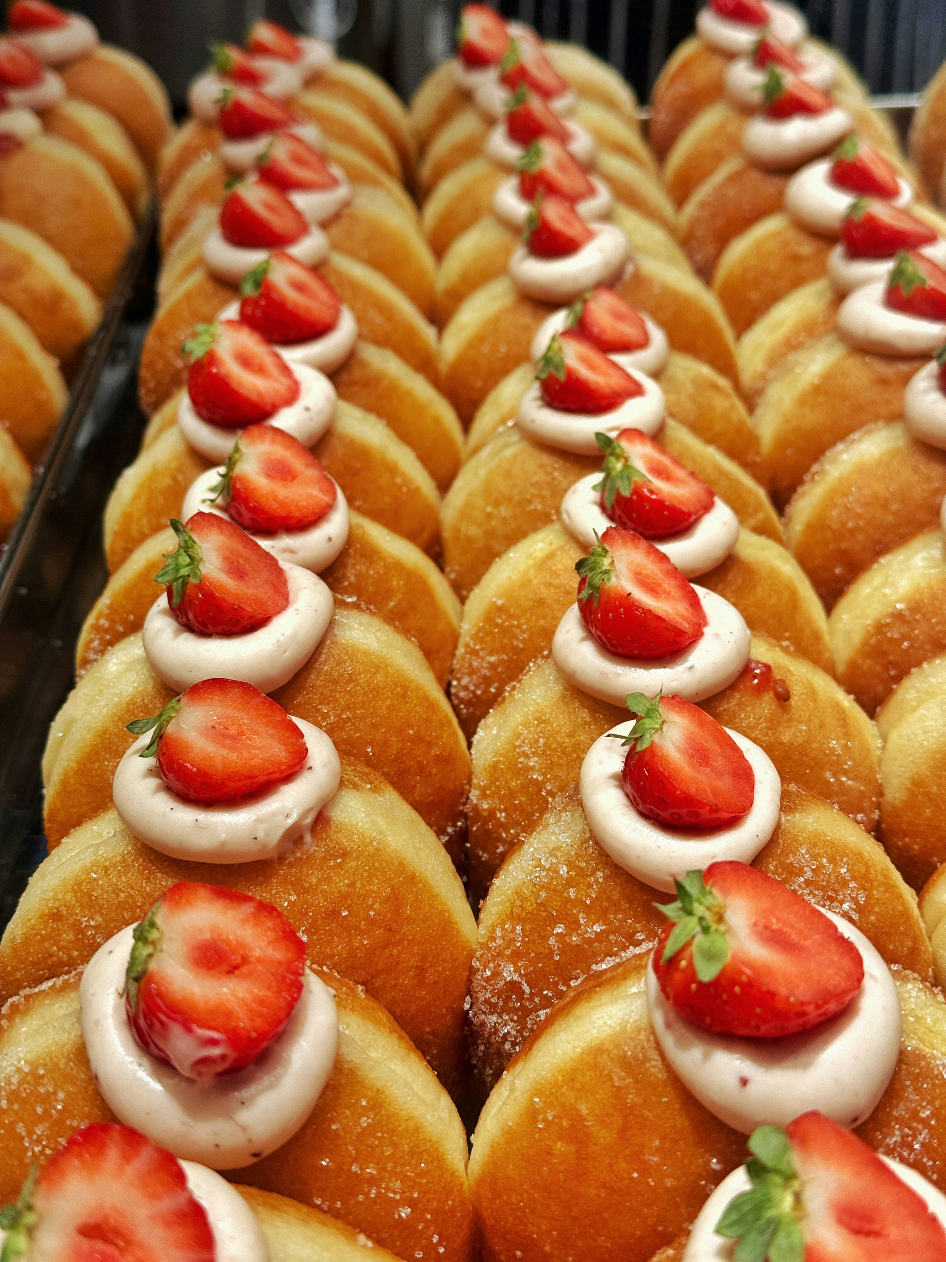 Rows of donuts topped with cream and strawberries