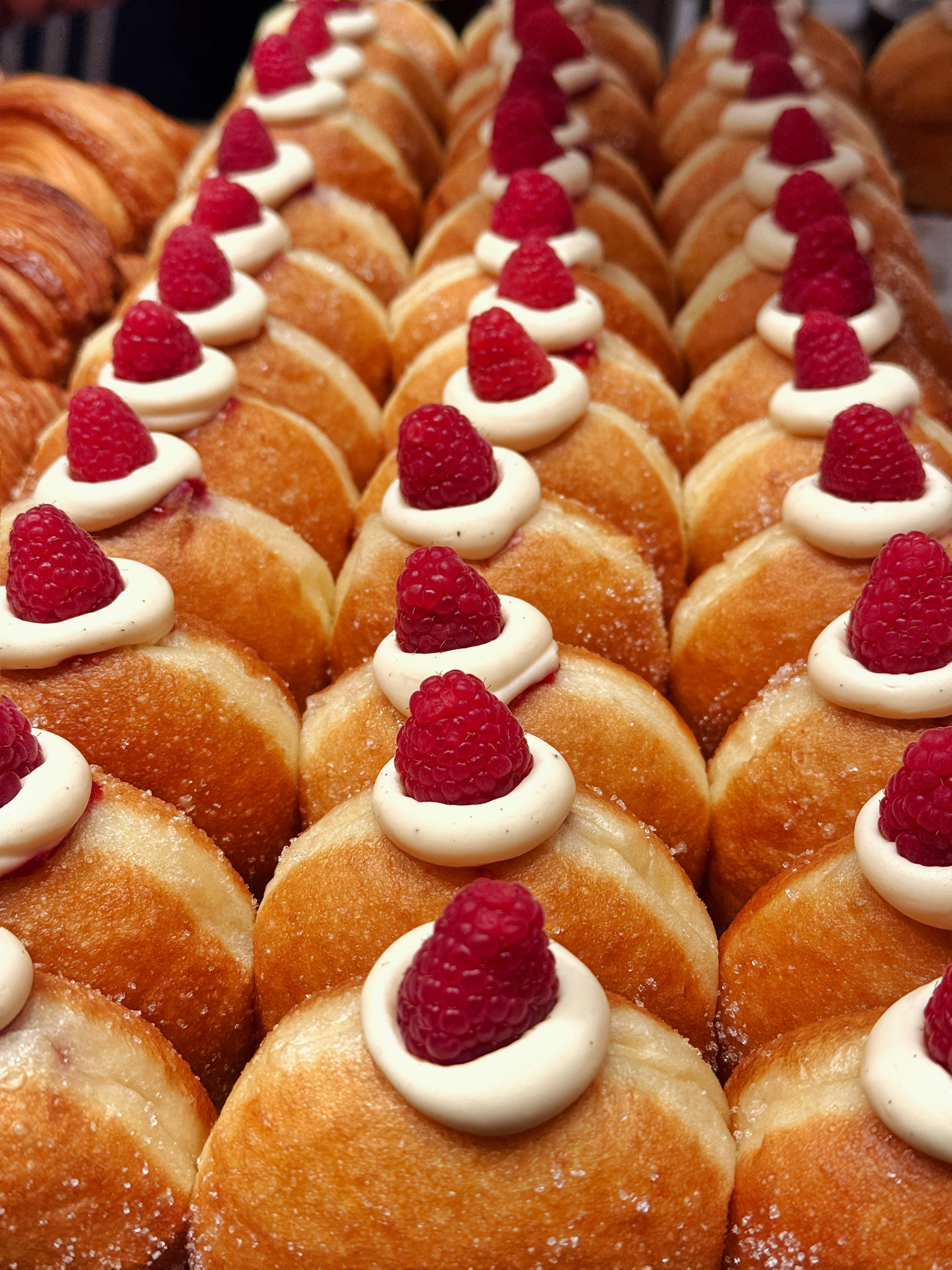 Rows of donuts topped with cream and raspberries