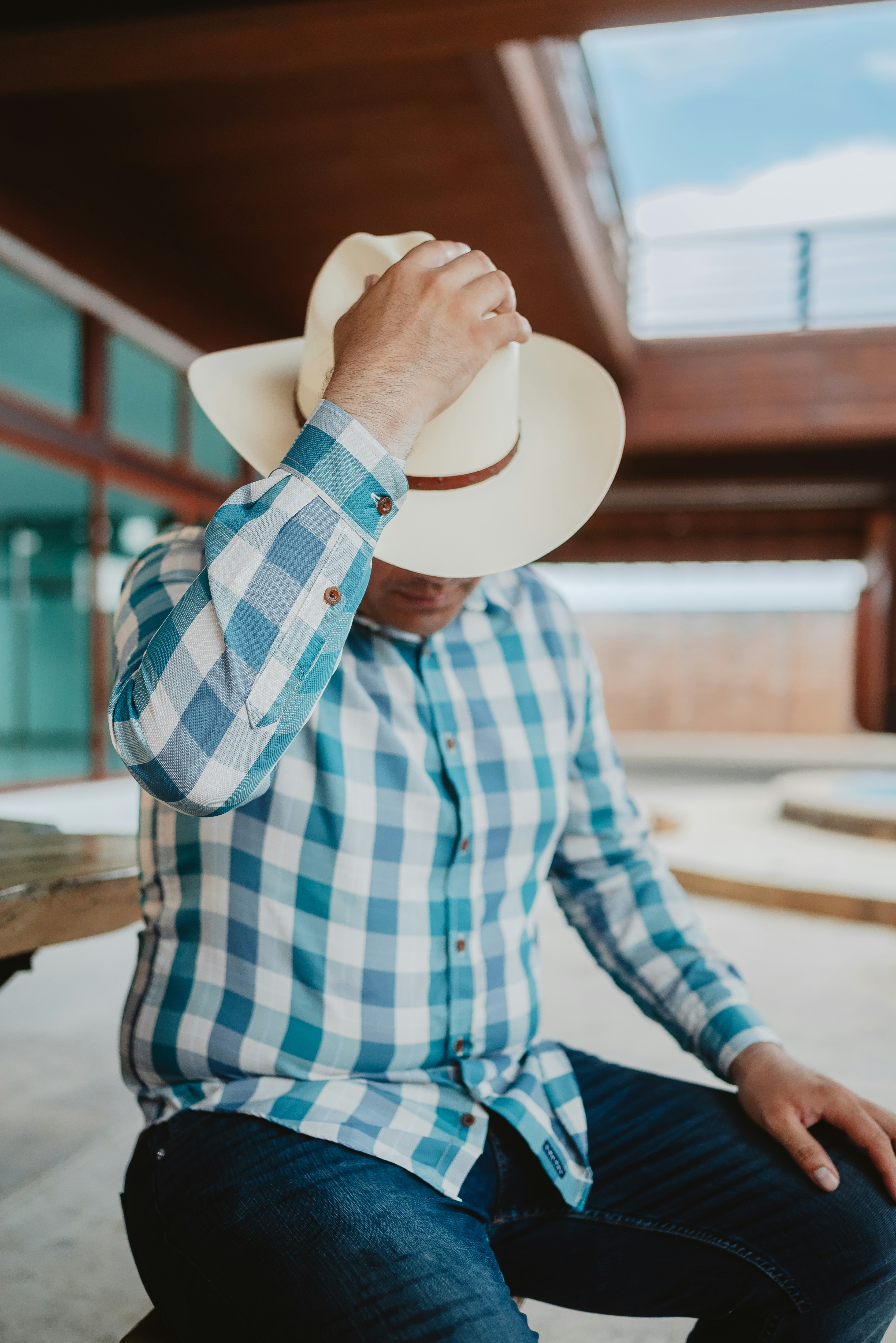Man in cowboy hat and plaid shirt sits outdoors