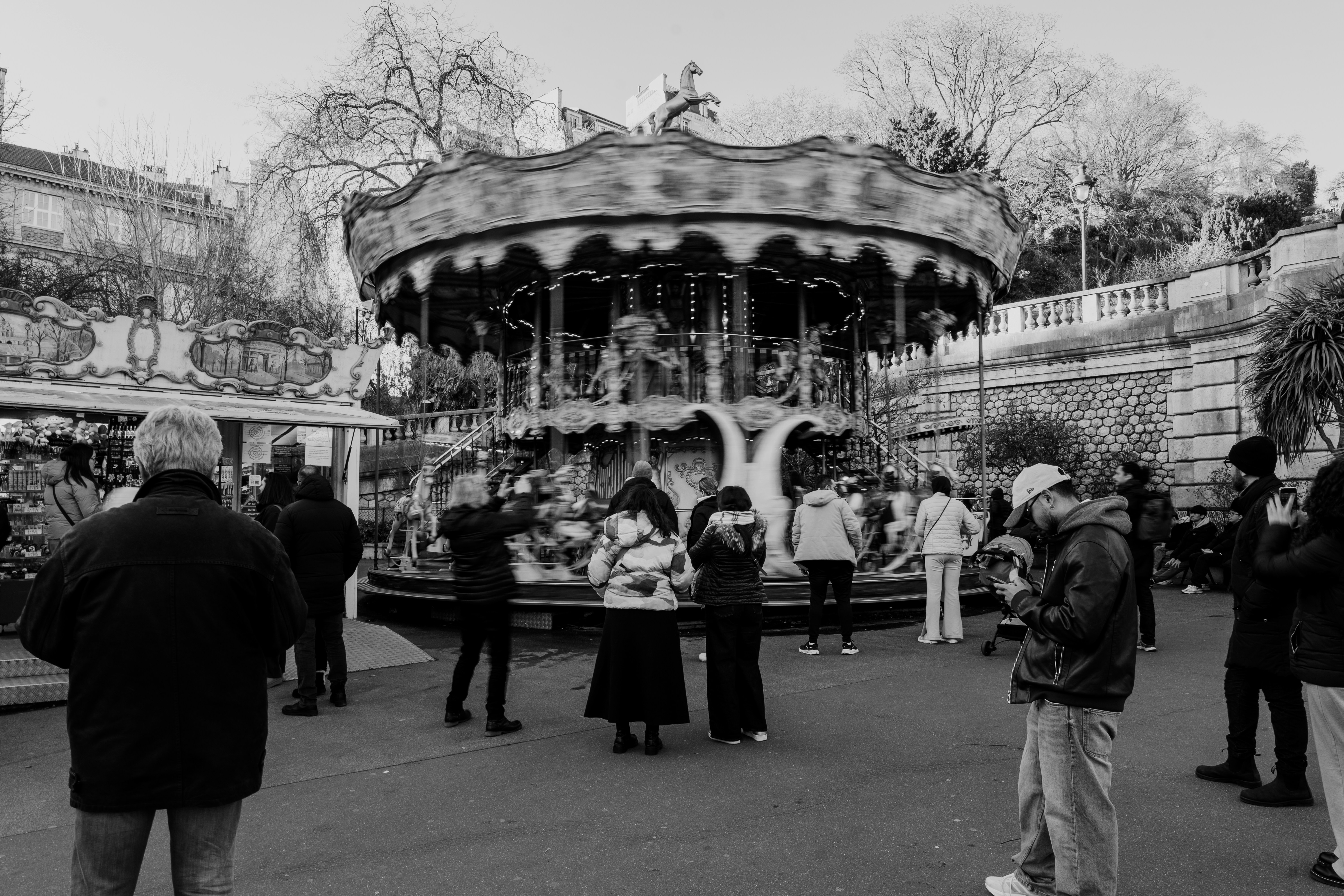 People gathered around a vintage carousel in a park.