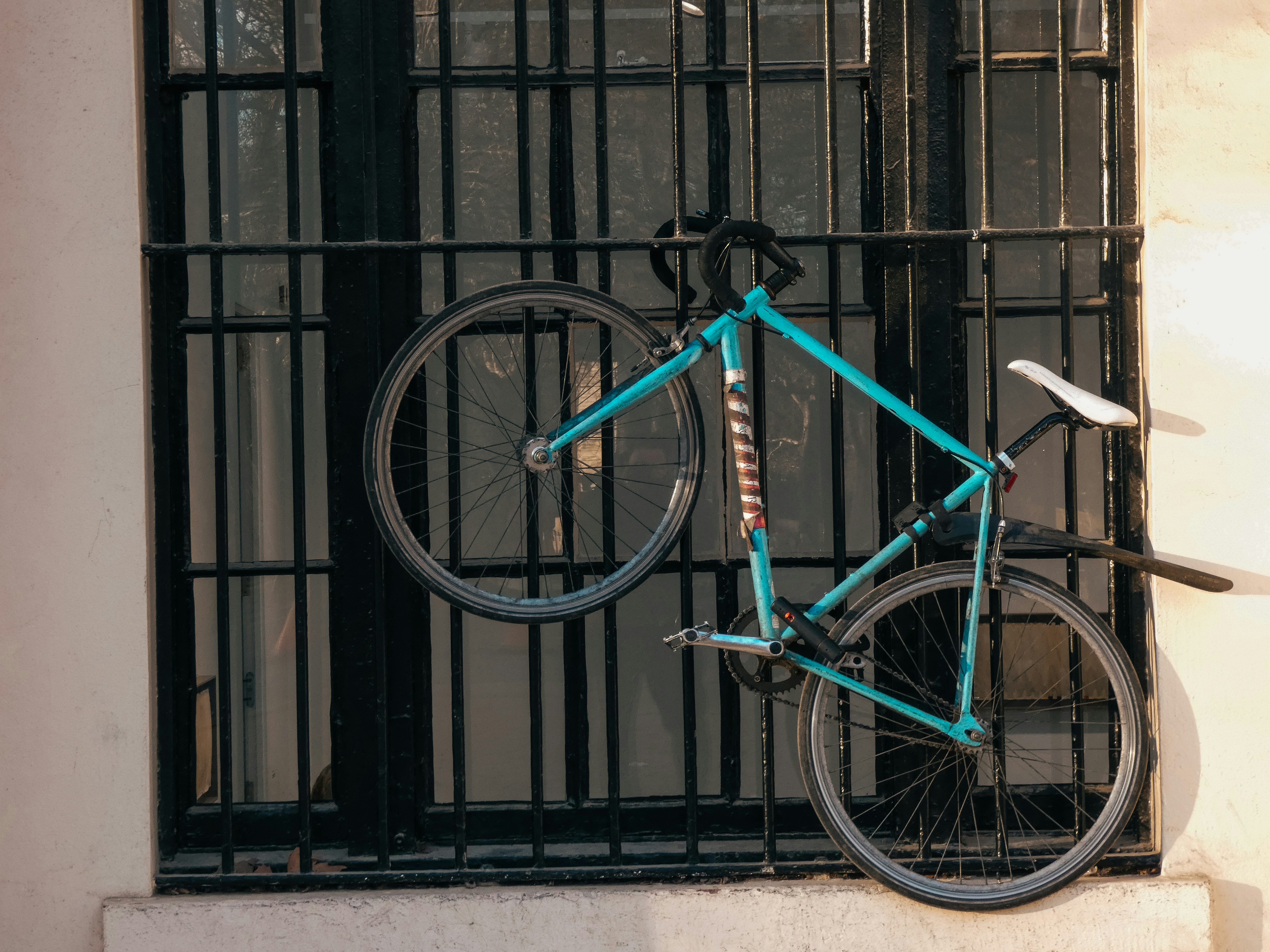 A turquoise bicycle rests against a barred window.
