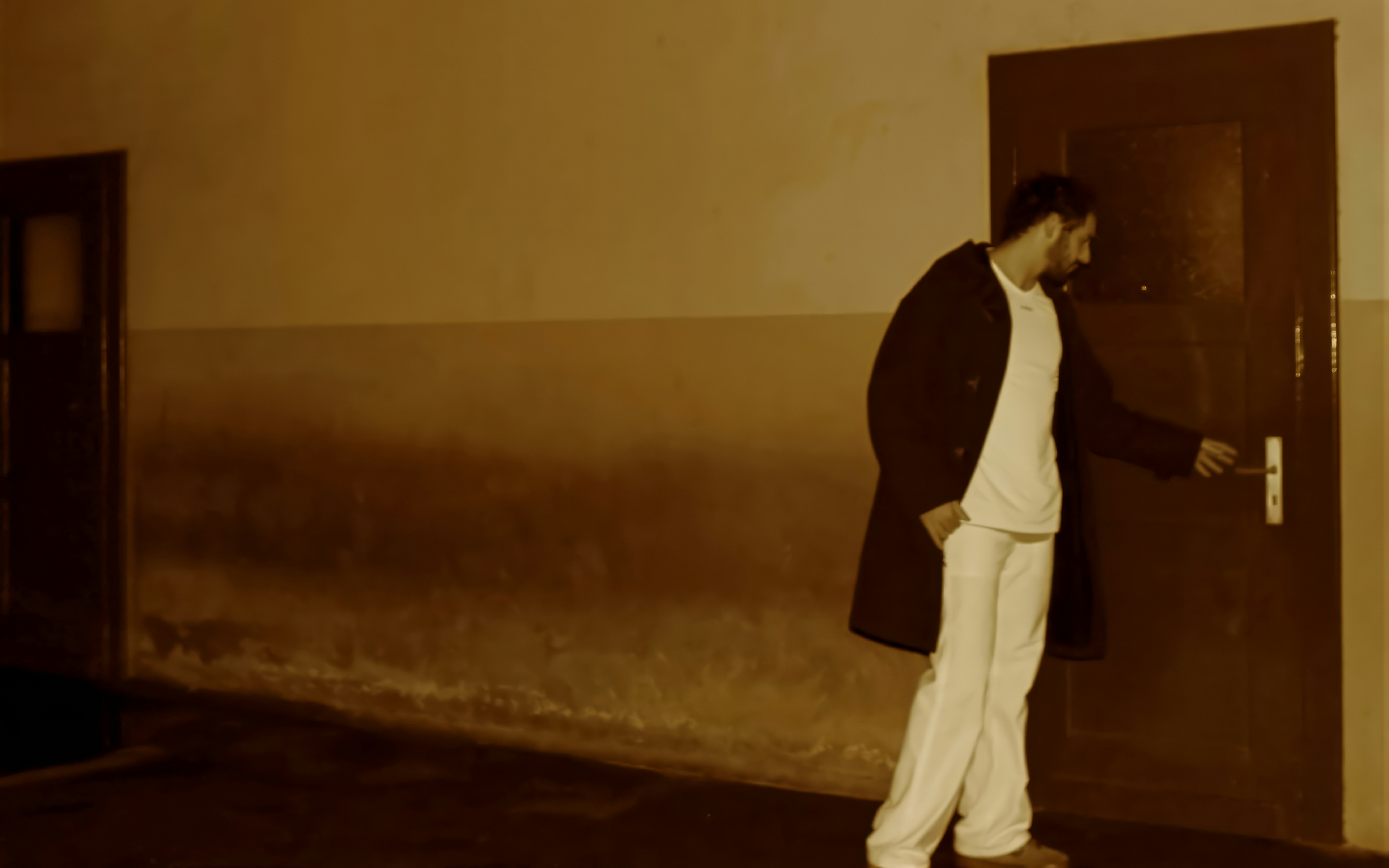 Man in coat opens a door in a hallway.