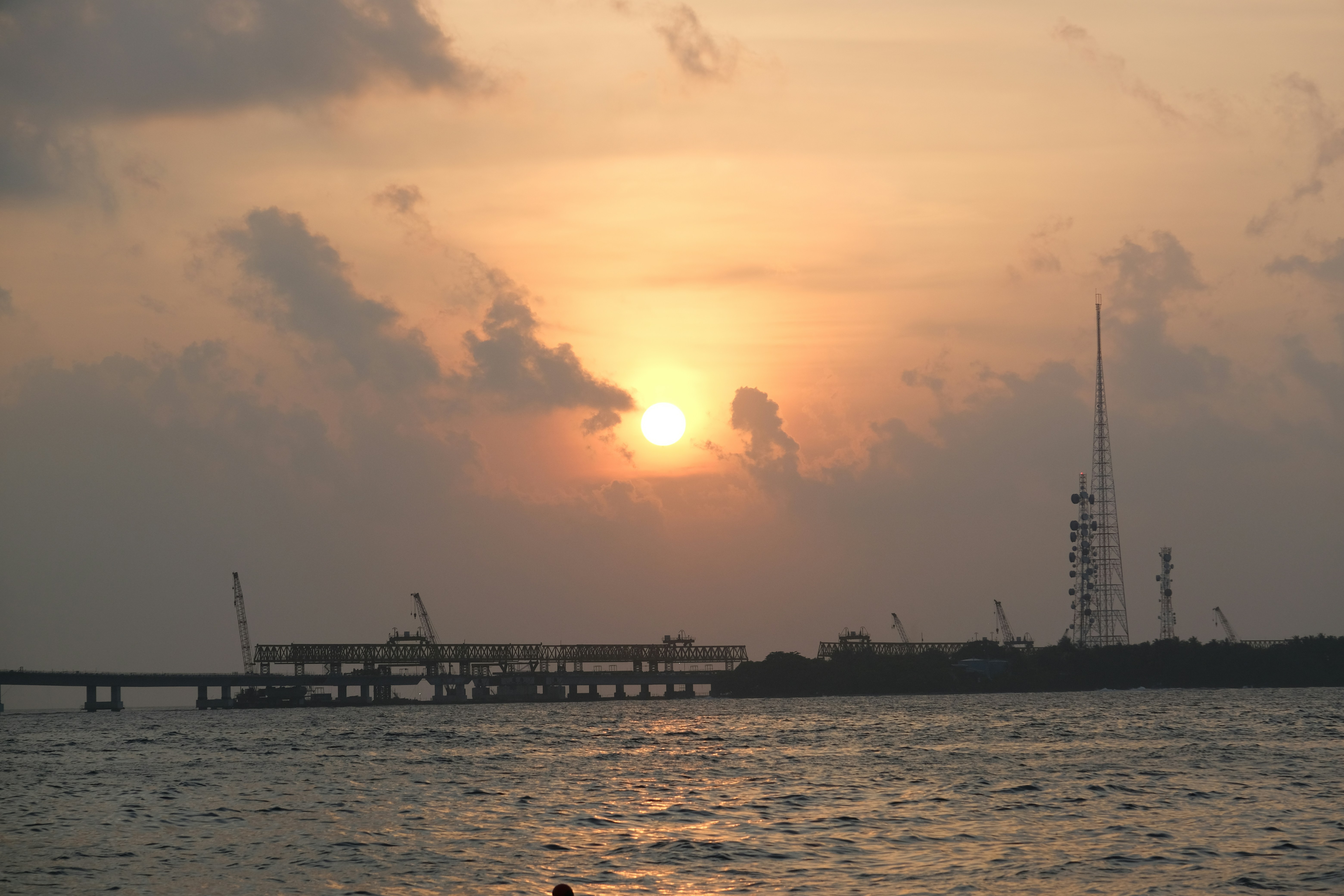 Sonnenuntergang über einem ruhigen Ozean mit Industriebauten.