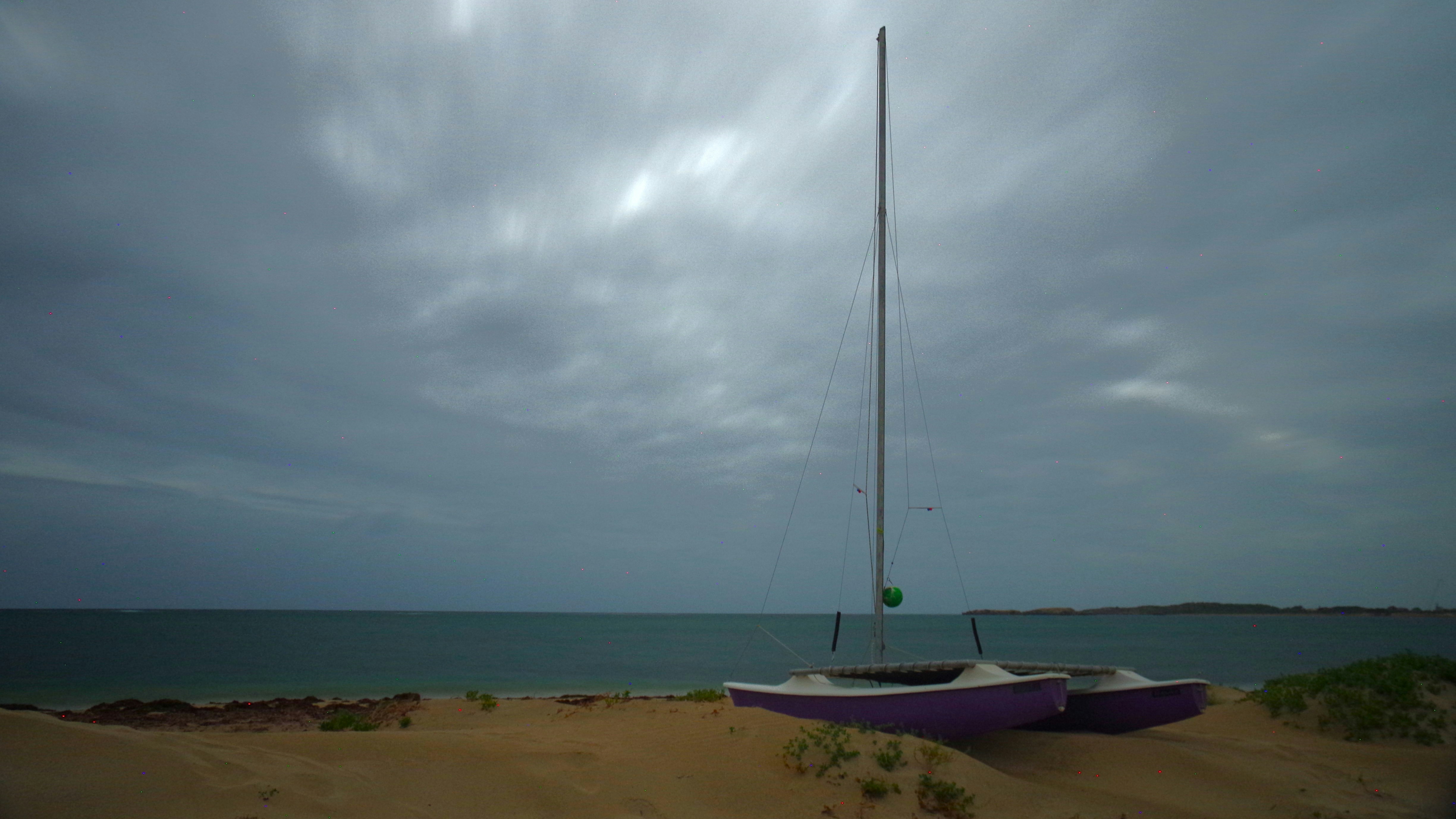Two sailboats rest on a sandy beach under cloudy skies.