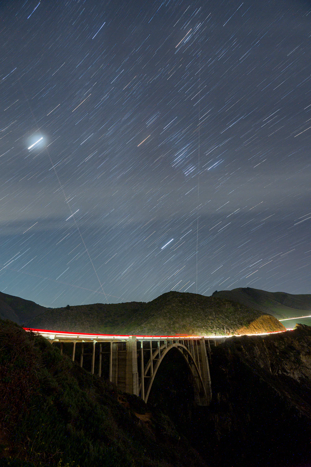 Long-exposure star trails circling over a bridge at night