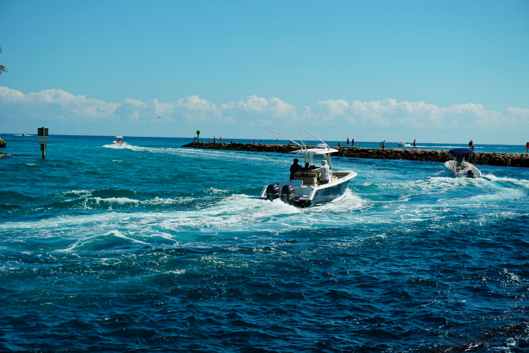 Boats running out through an inlet beside a rock jetty