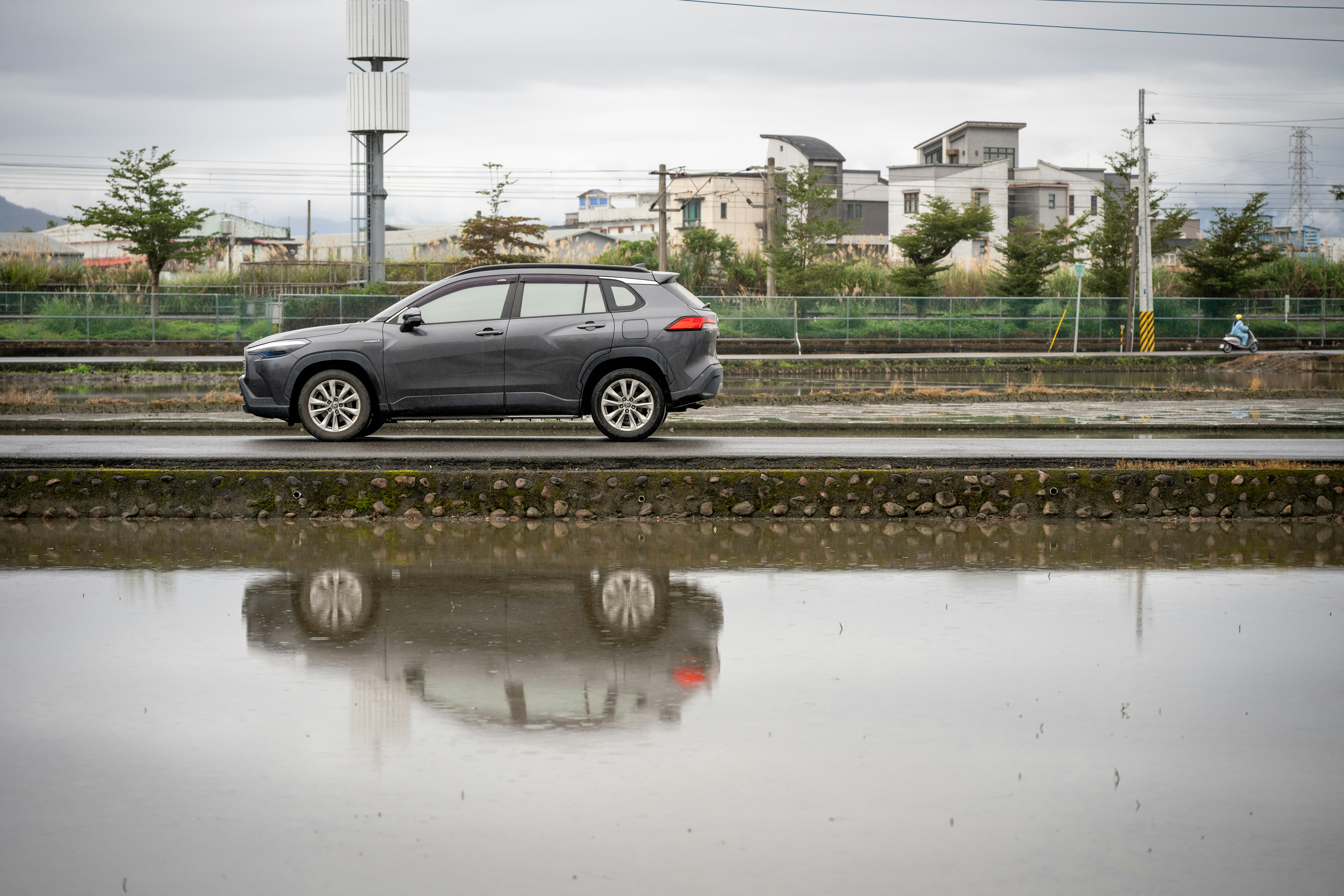 Graues Auto fährt an einem überfluteten Feld mit Spiegelung vorbei