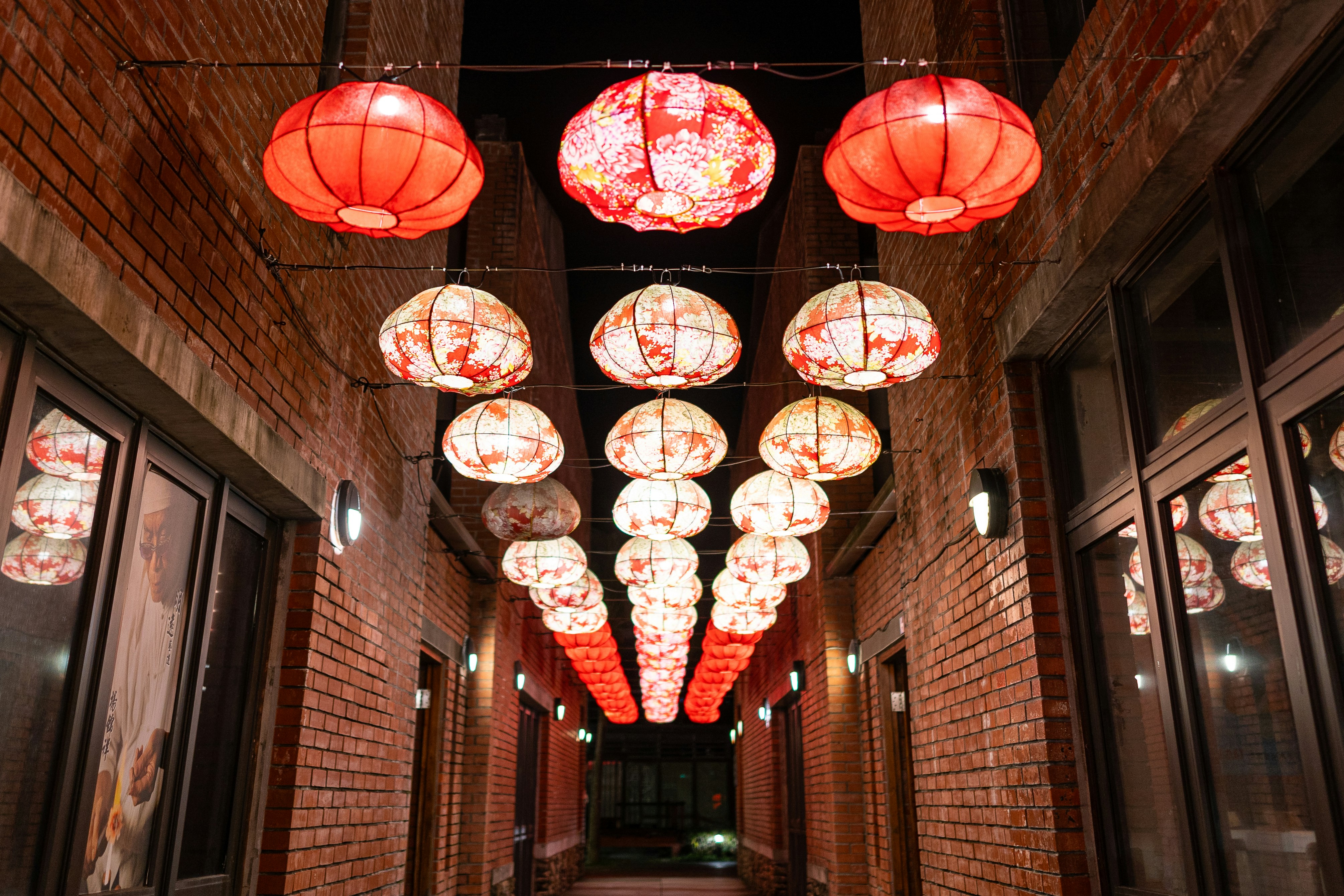 Red and white lanterns illuminate a brick alleyway at night
