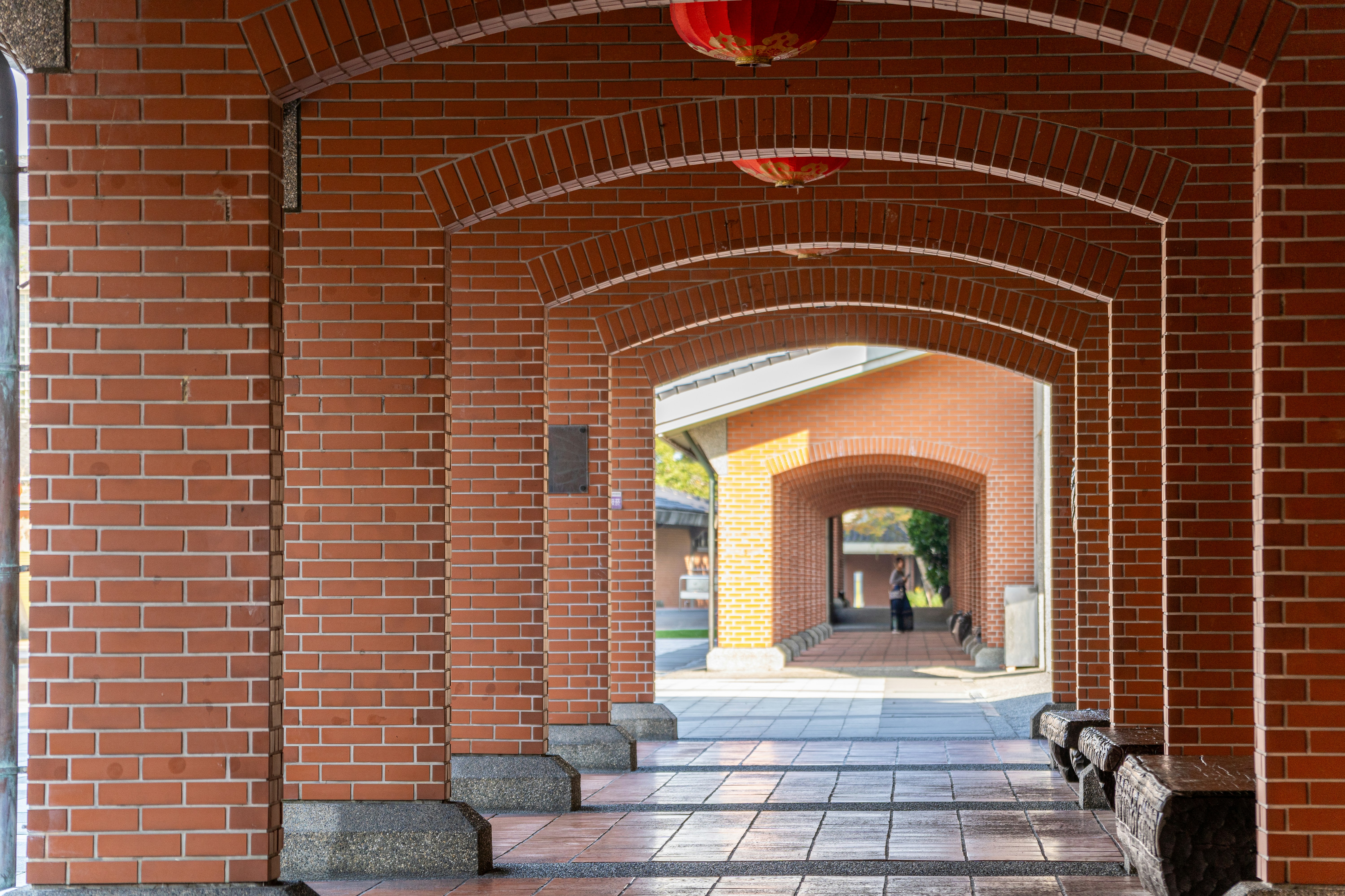Red brick arches lead to a sunlit courtyard.