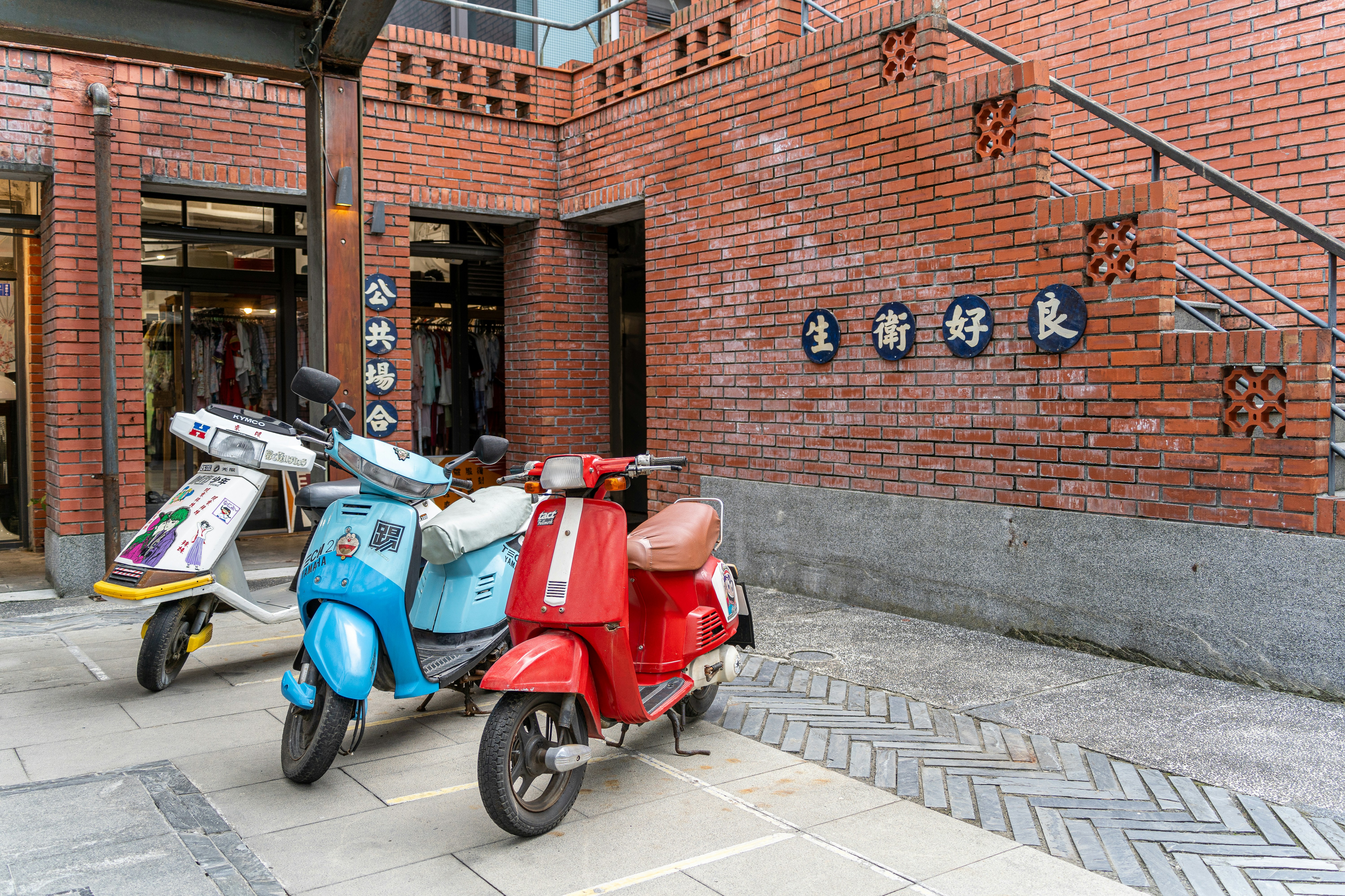 Three colorful scooters parked outside a brick building.