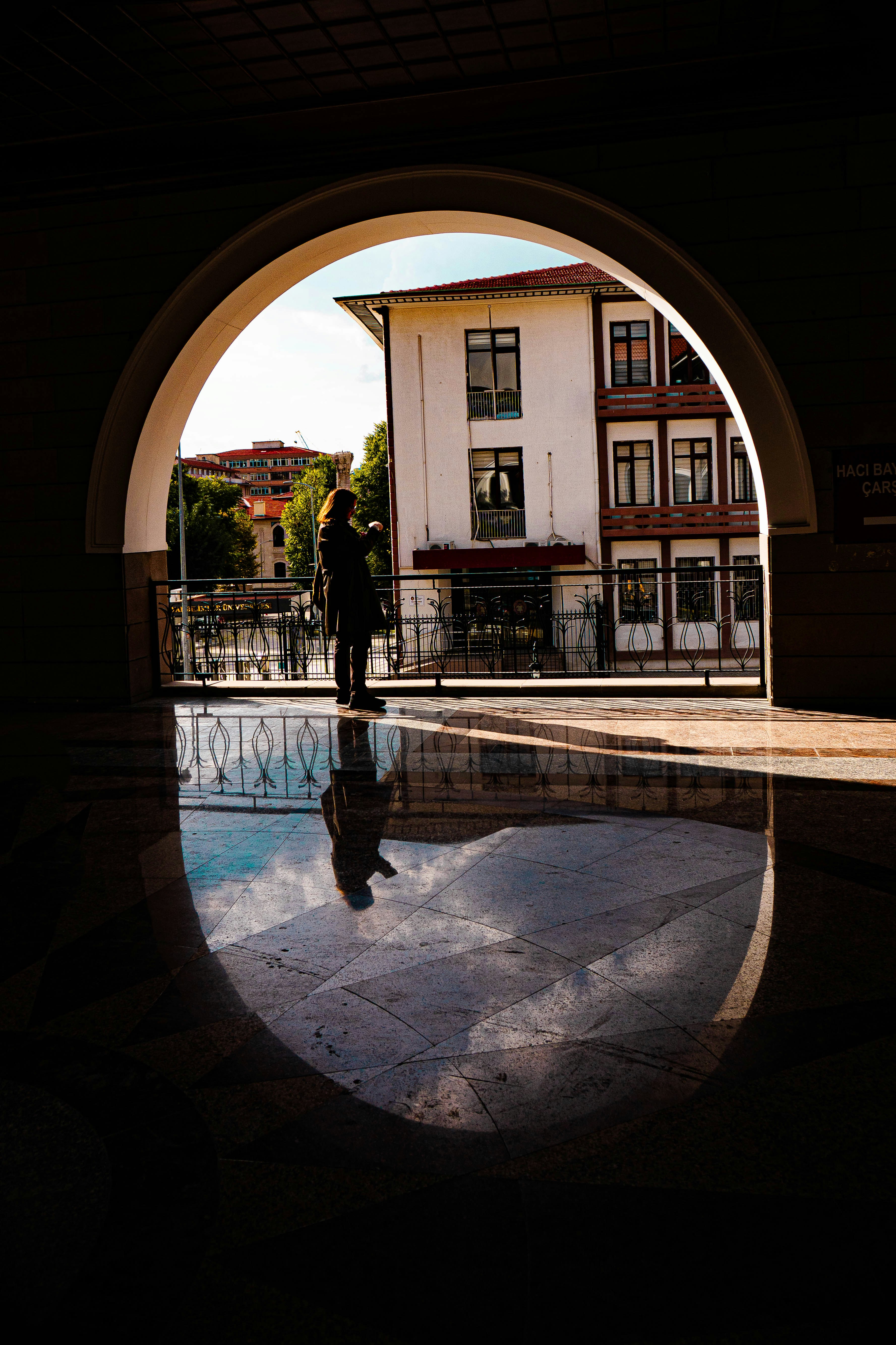 Woman reflected in wet pavement under an archway.