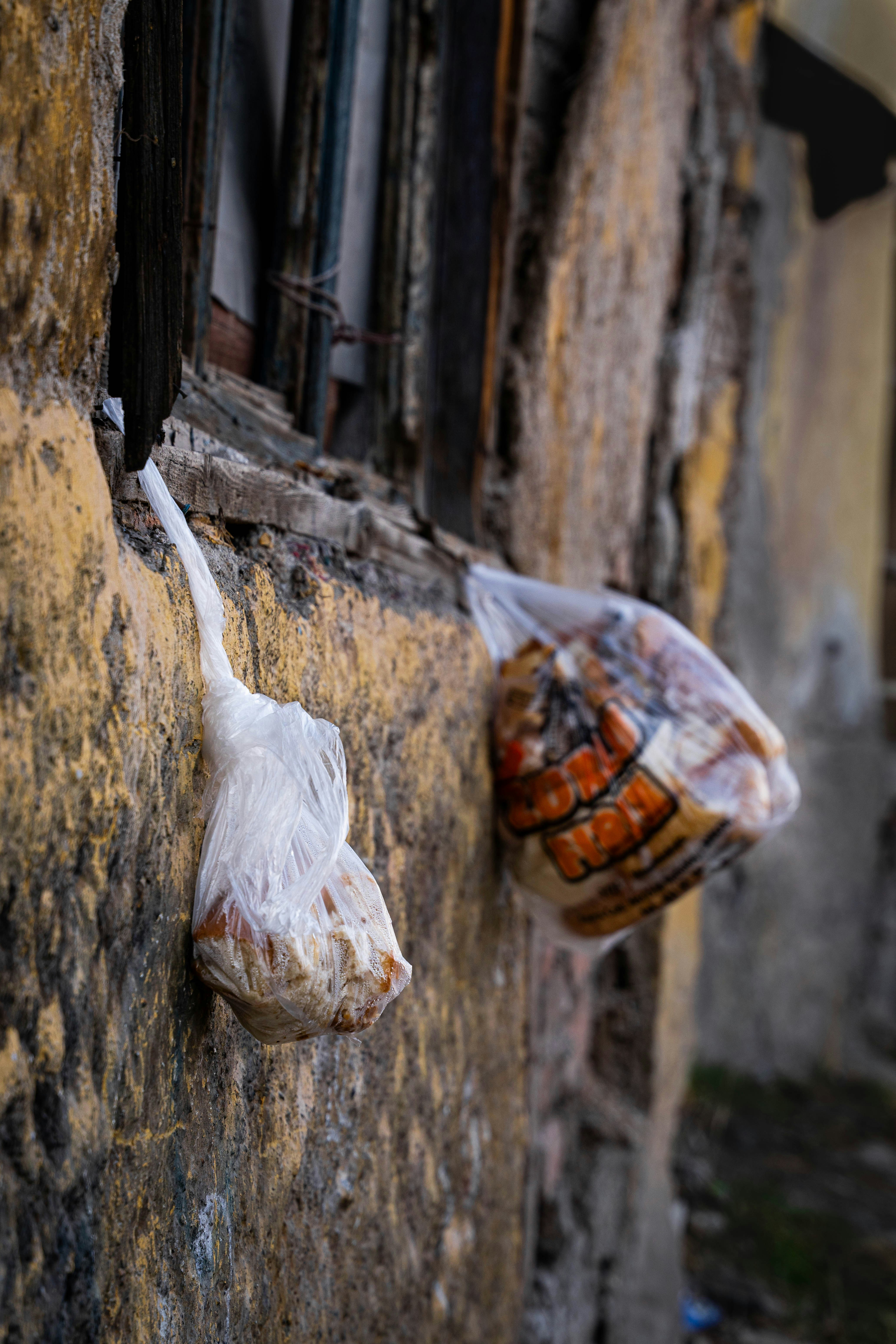 Two plastic bags of food hanging on a wall.