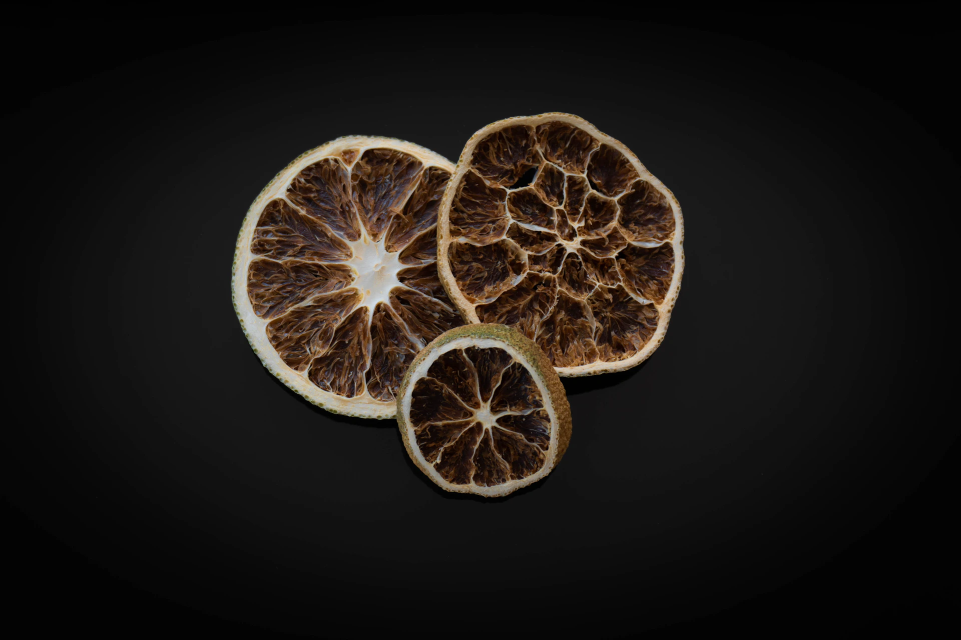 Three dried citrus slices on a black background