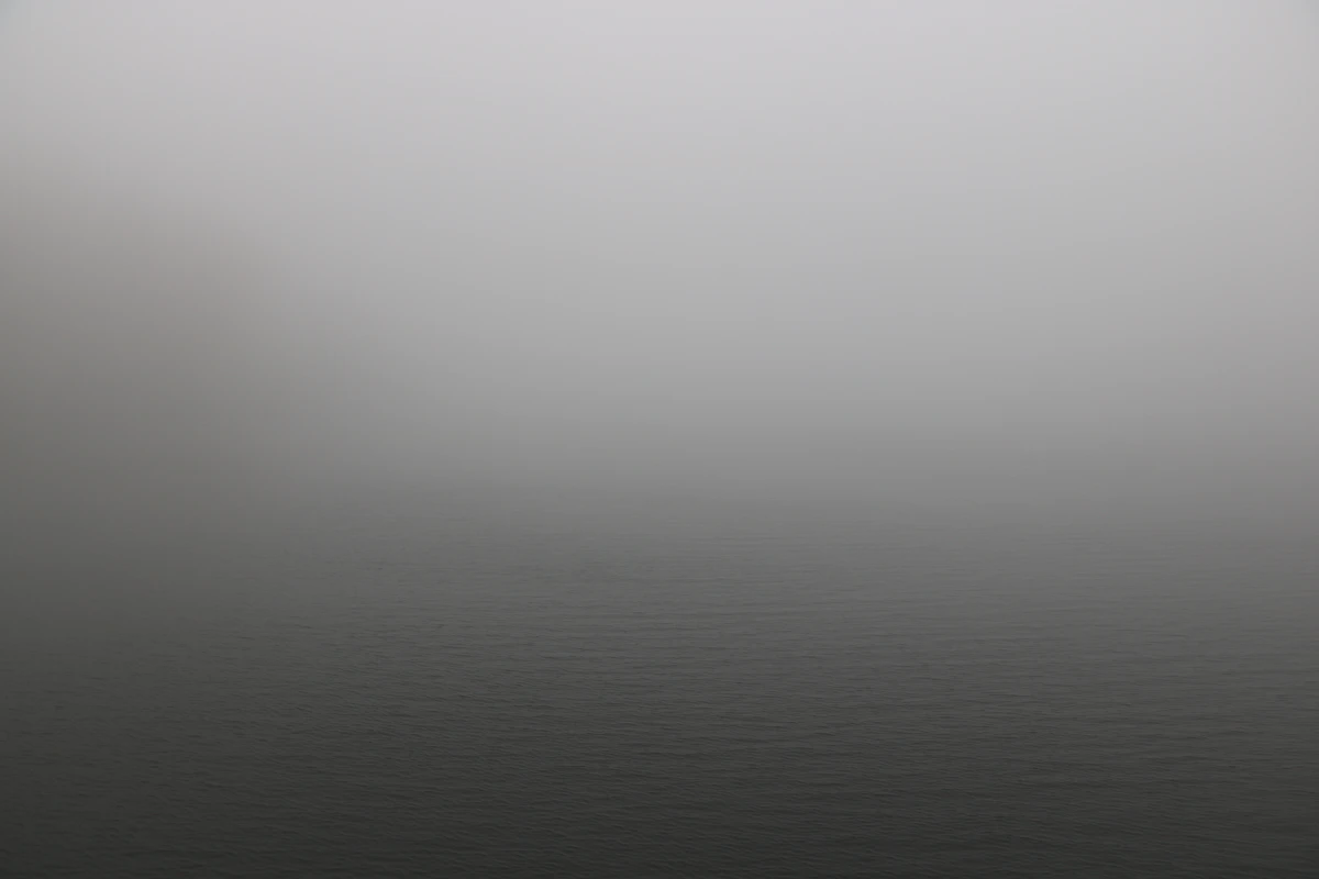 A soft grey gradient of fog over still water, with no horizon to hold on to