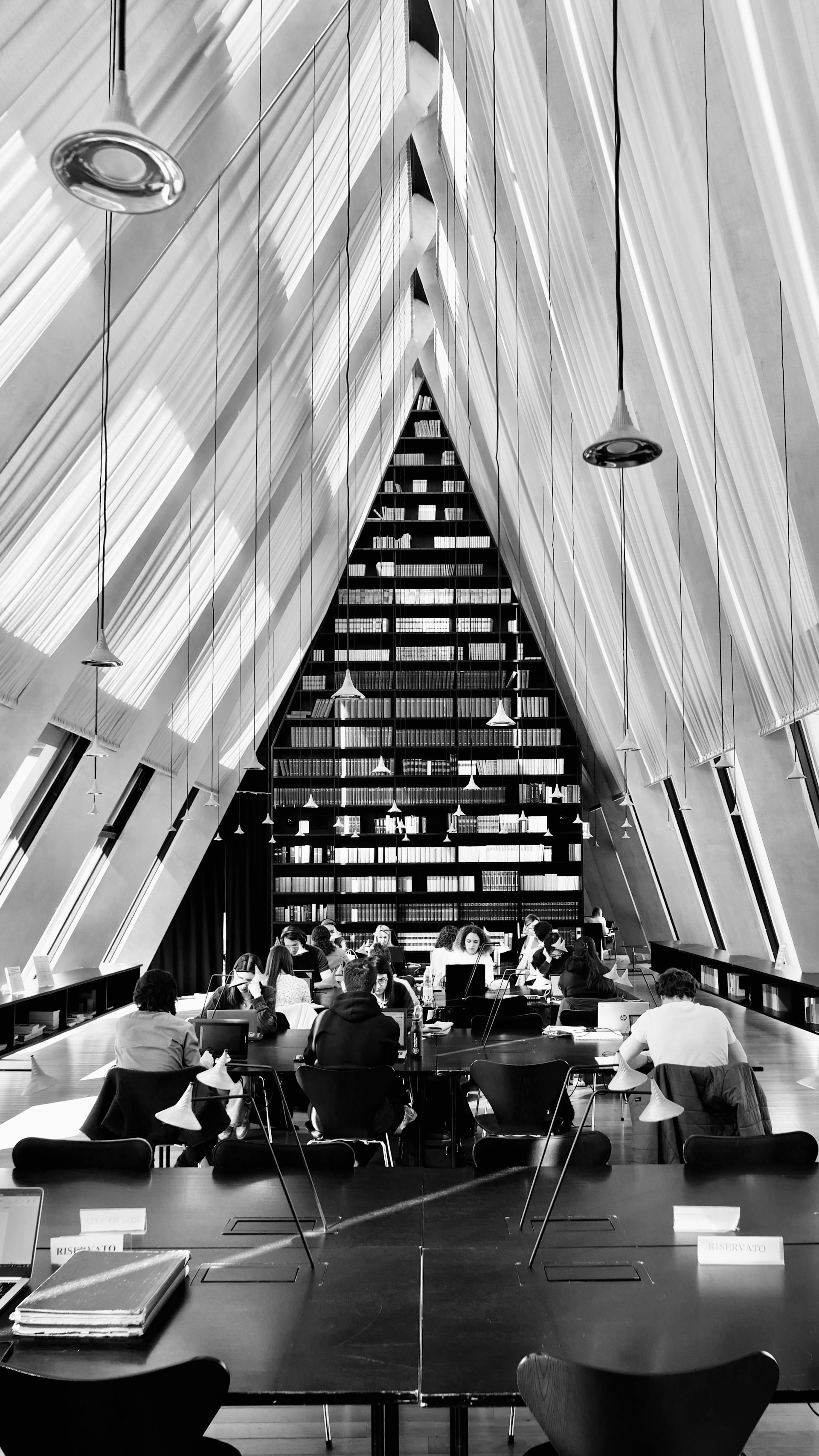 People studying at tables in a modern library with bookshelves.