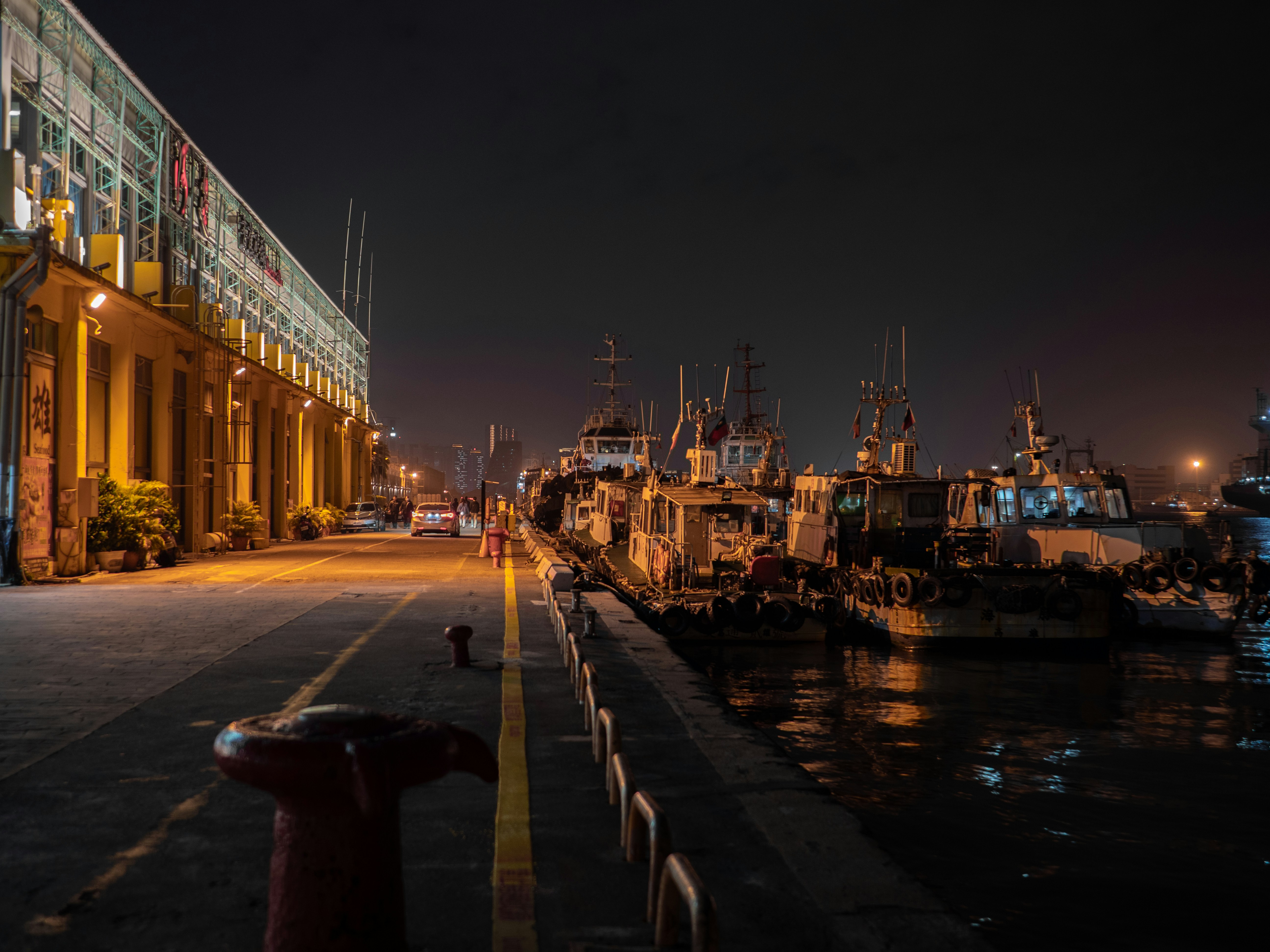 Boats docked at a harbor with illuminated buildings at night.