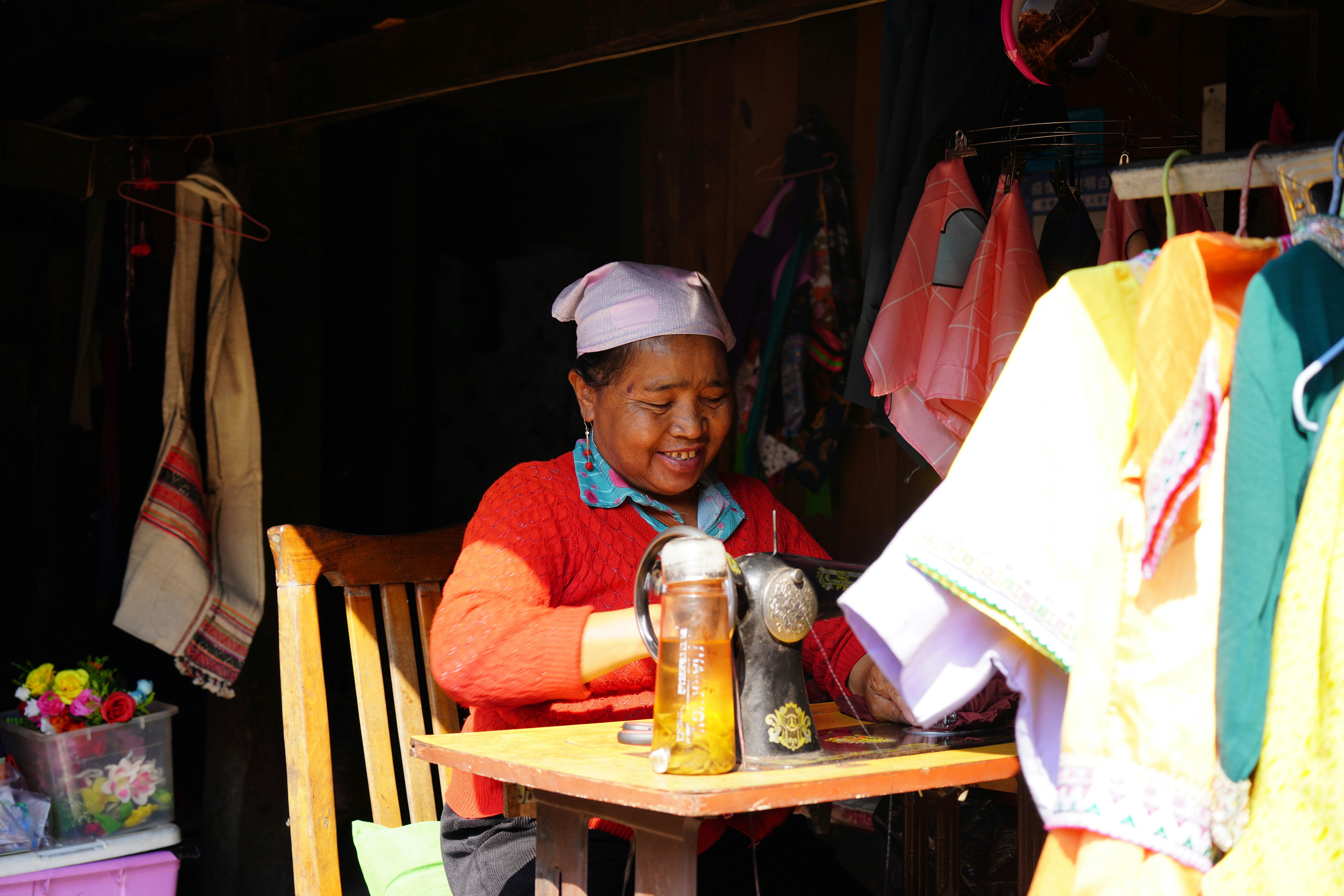Elderly woman sewing at a machine with colorful clothes