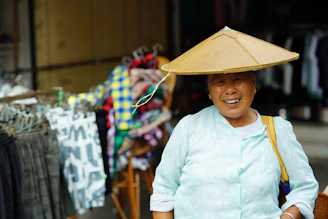 Elderly woman wearing a conical hat smiles.
