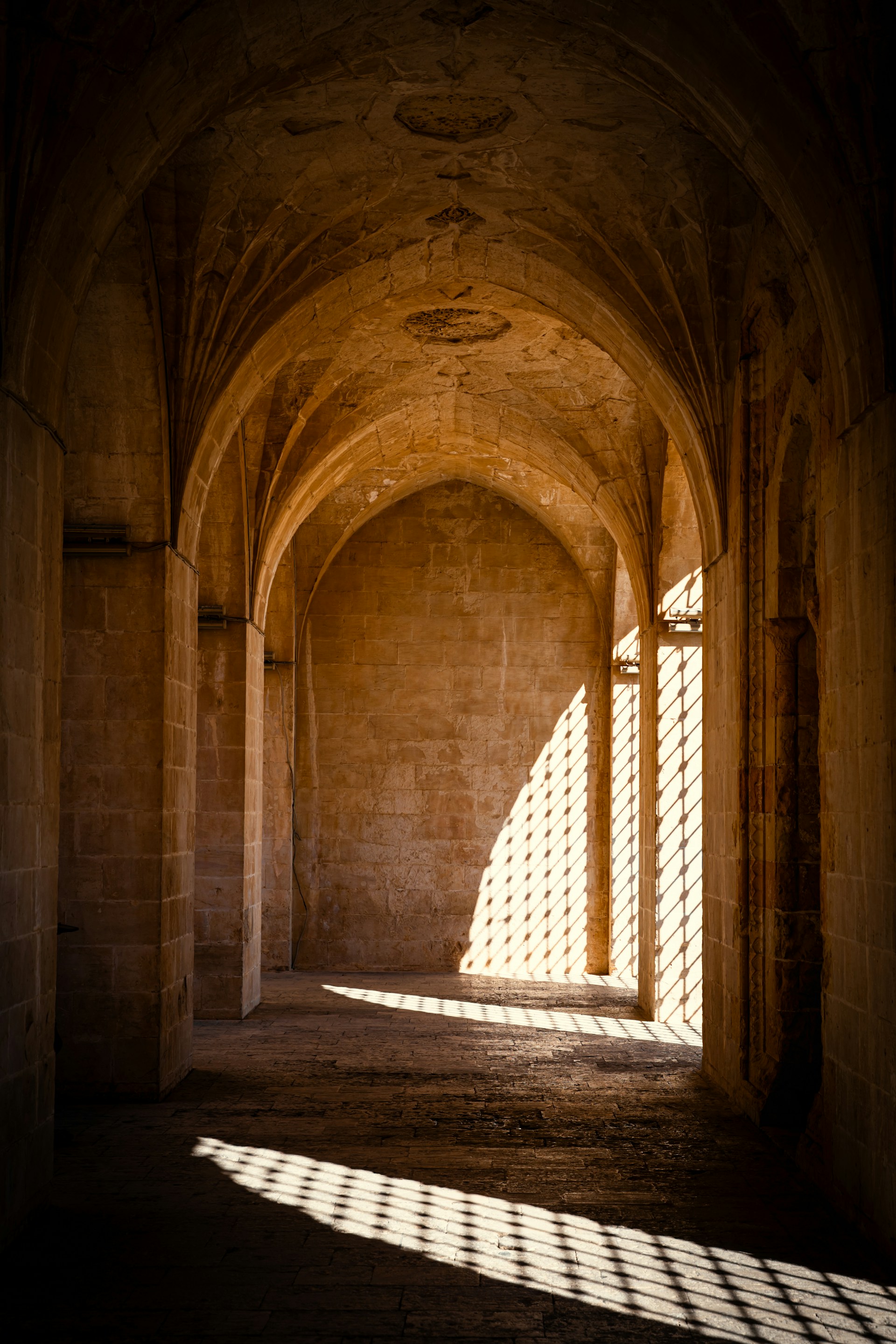 Sunlight streams through a patterned window into an arched hall