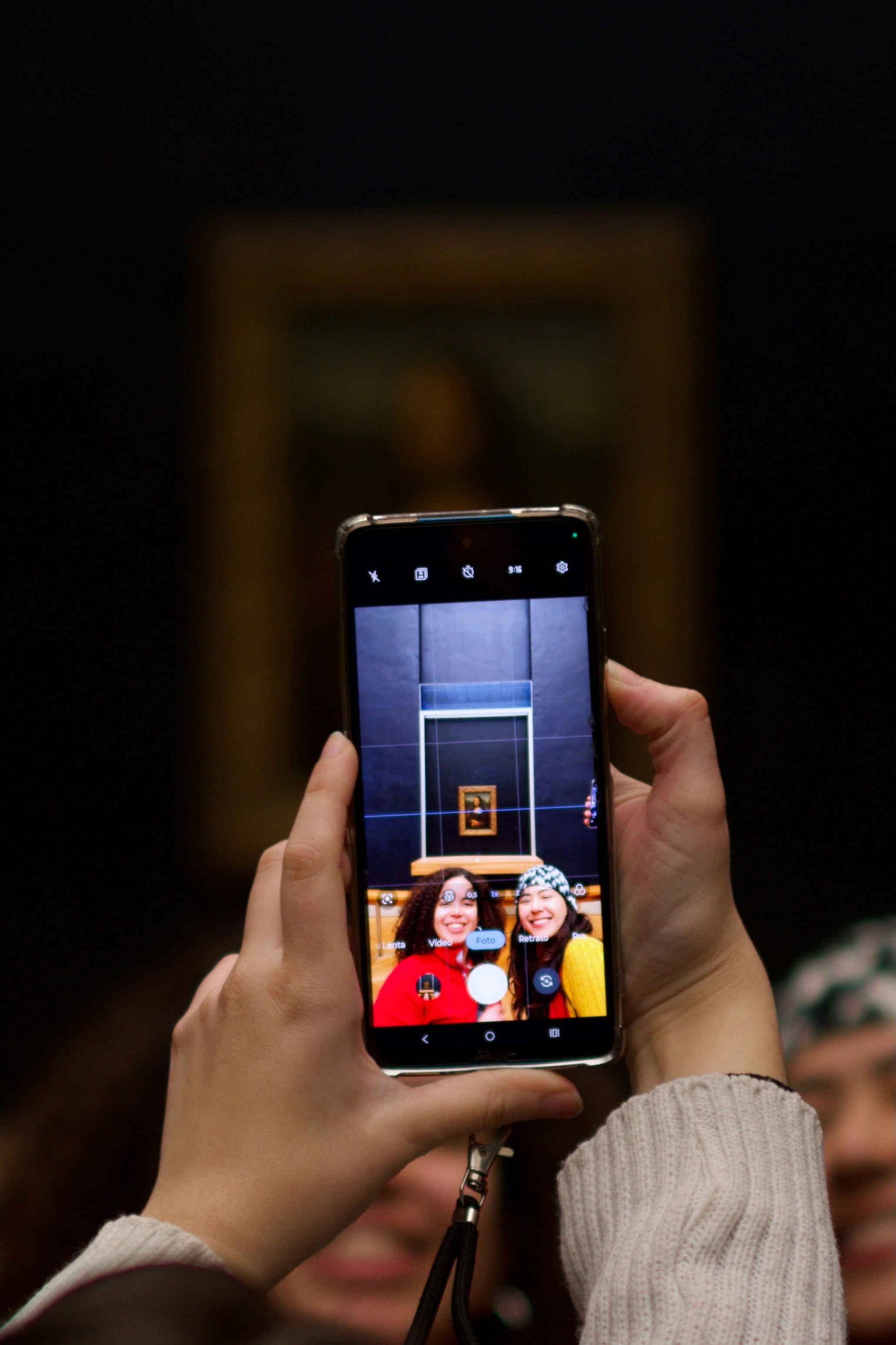 Two women take a selfie in front of a painting.