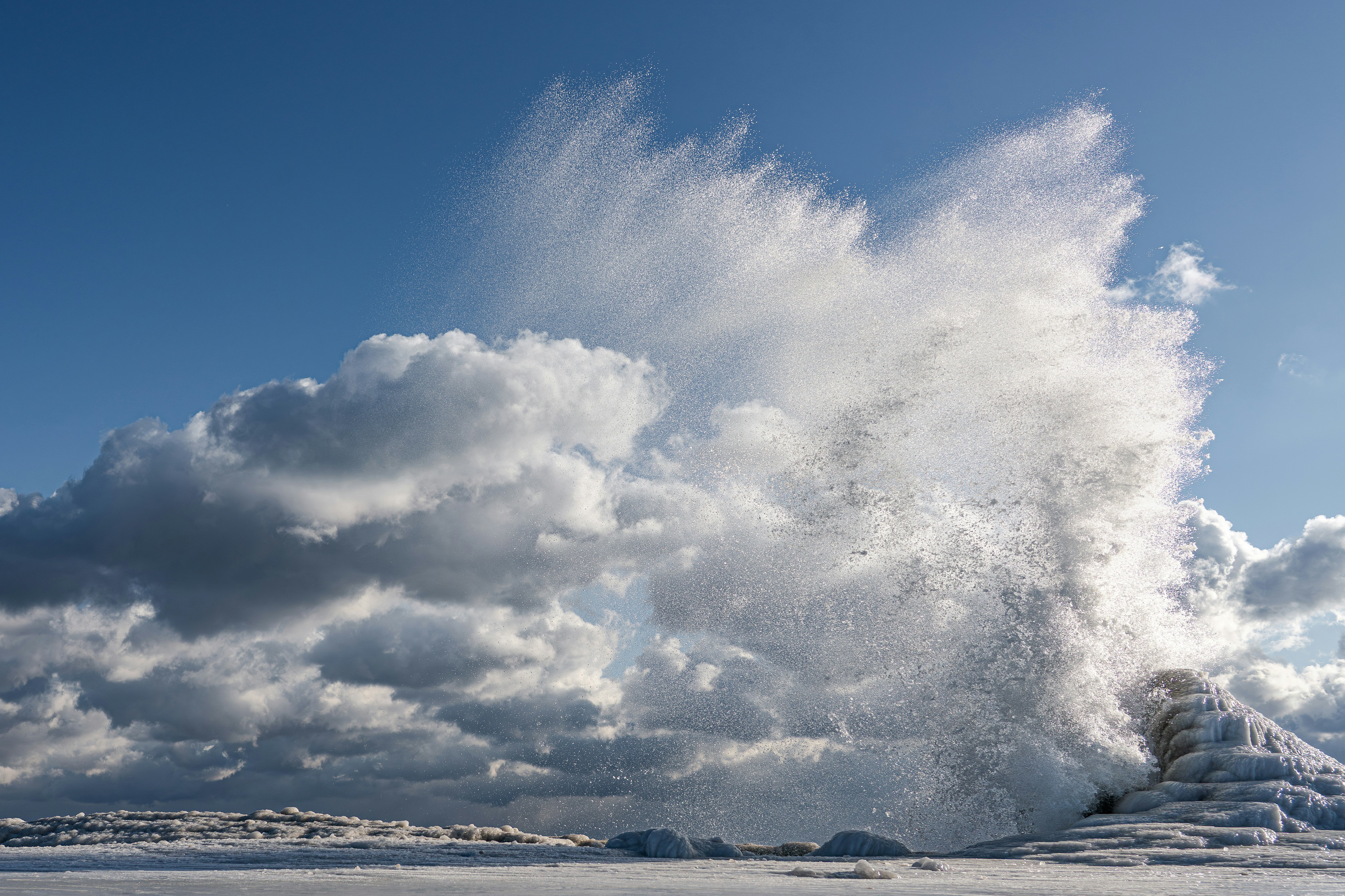 Vague de l’océan s’écrasant contre rivage glacé sous un ciel bleu